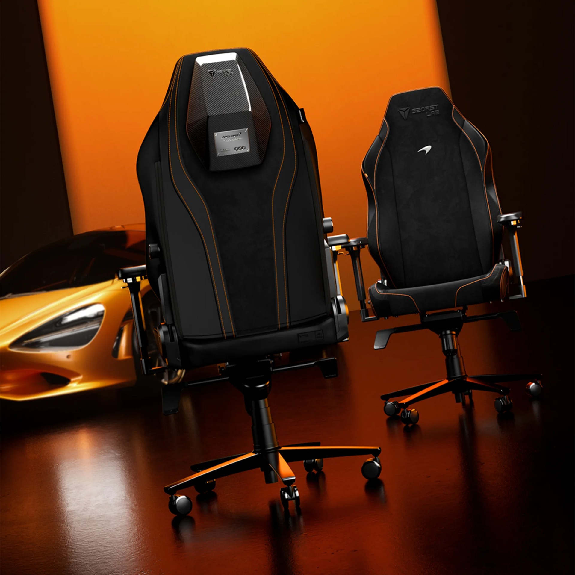 Two black gaming chairs with orange stitching and logos, positioned in front of an orange sports car and backdrop.