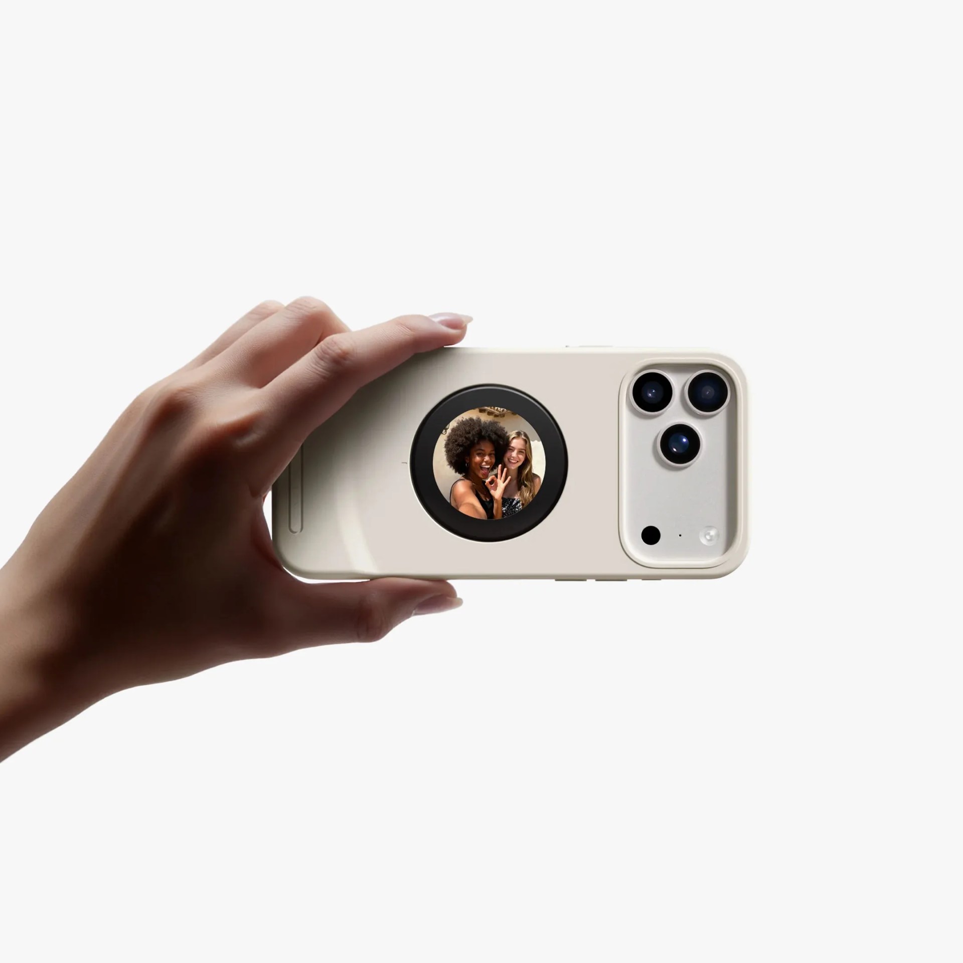 Hand holding a beige smartphone with three rear cameras and a circular secondary screen showing a selfie of two smiling people.