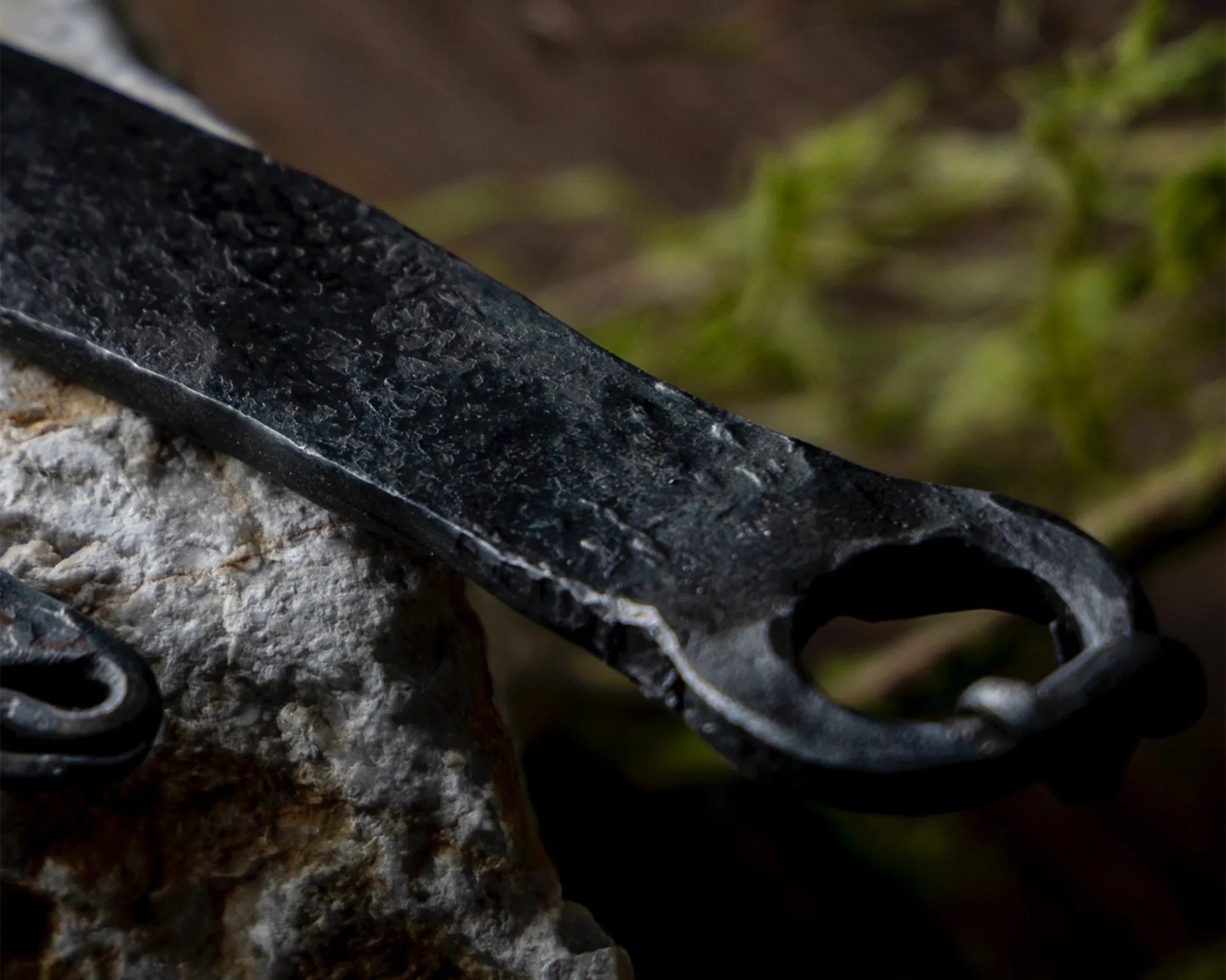 Close-up of a textured black metal tool with a circular opening resting on a rough stone surface.