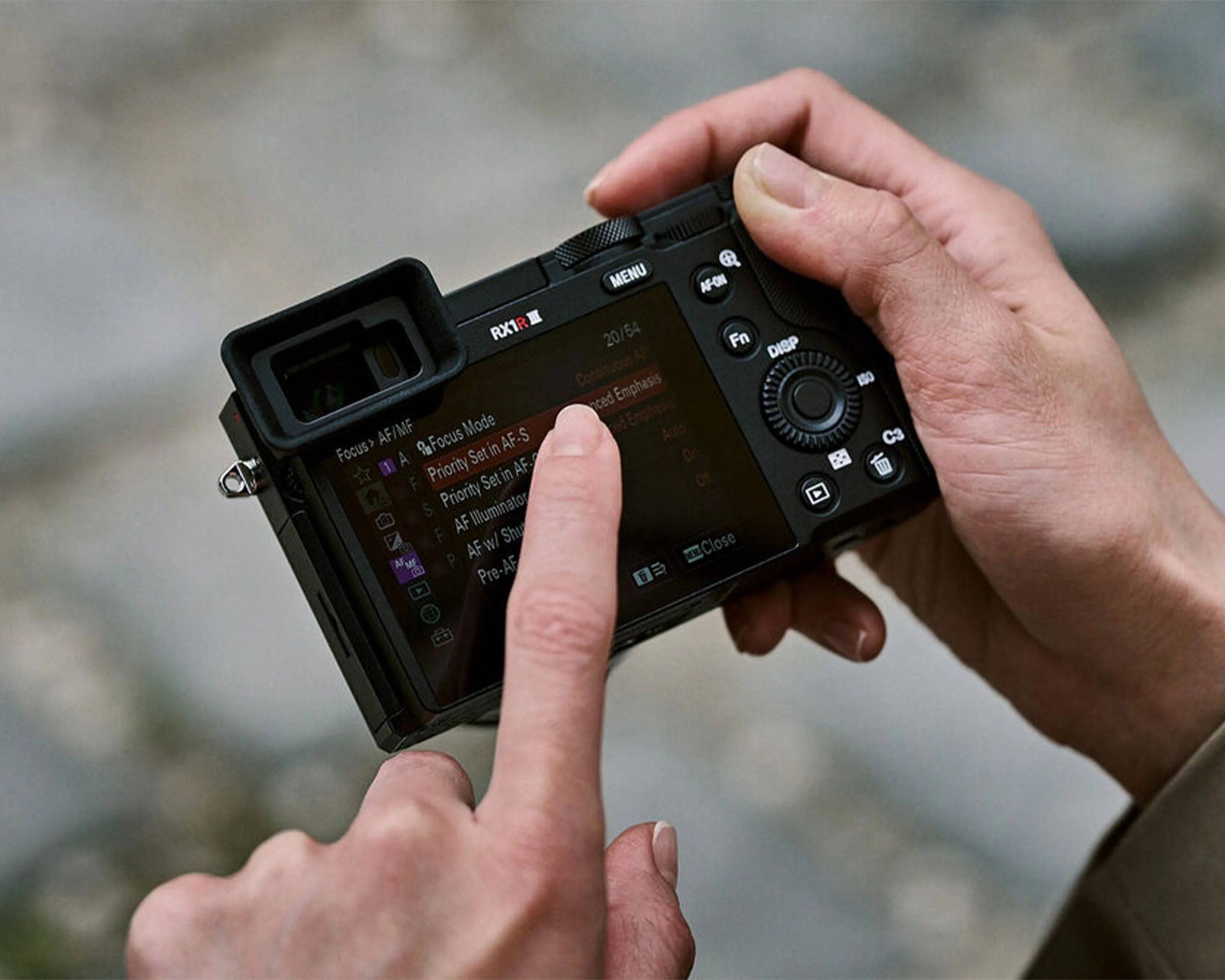 Person adjusting focus settings on the rear touchscreen of a black Sony RX1R III camera.