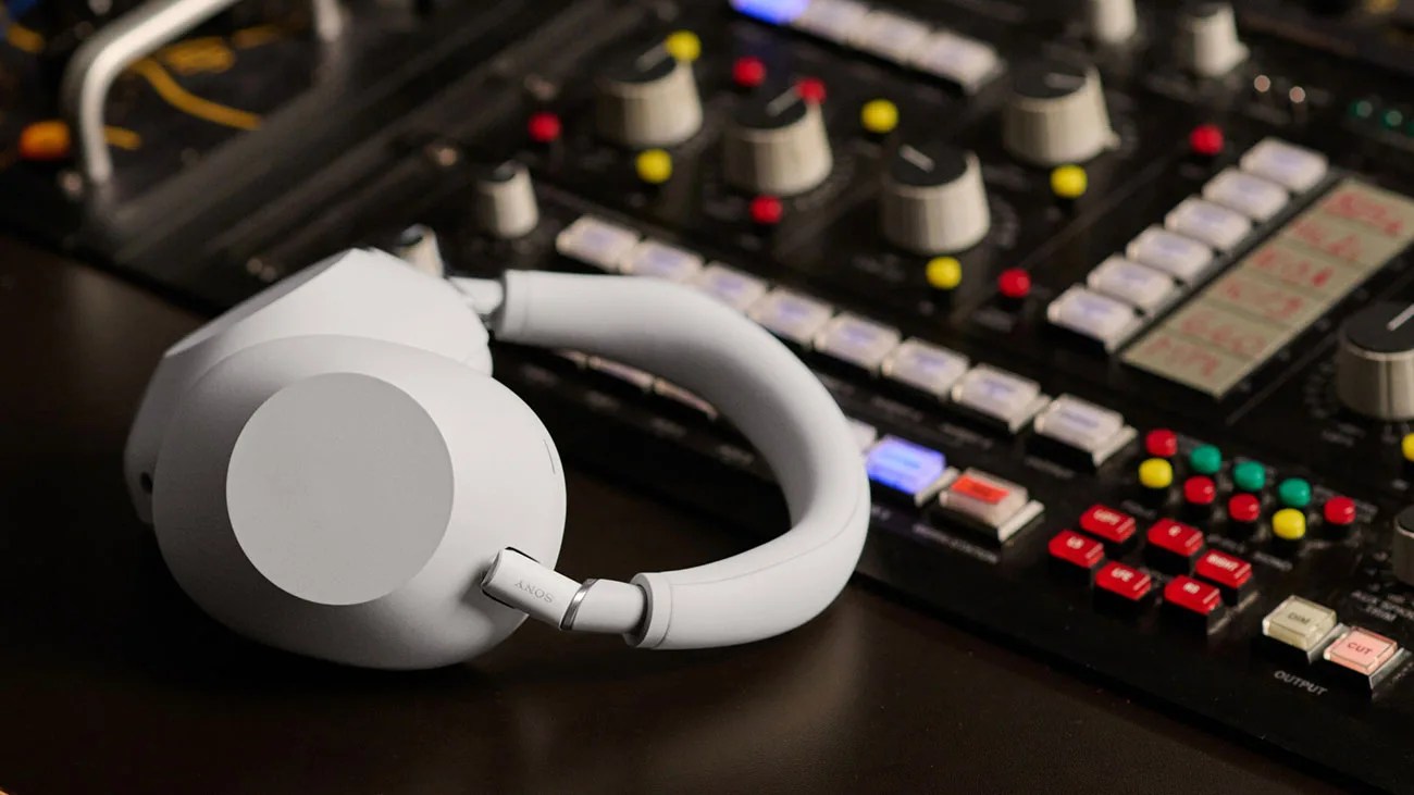 White Sony wireless over-ear headphones resting on a dark surface near an audio mixing console.
