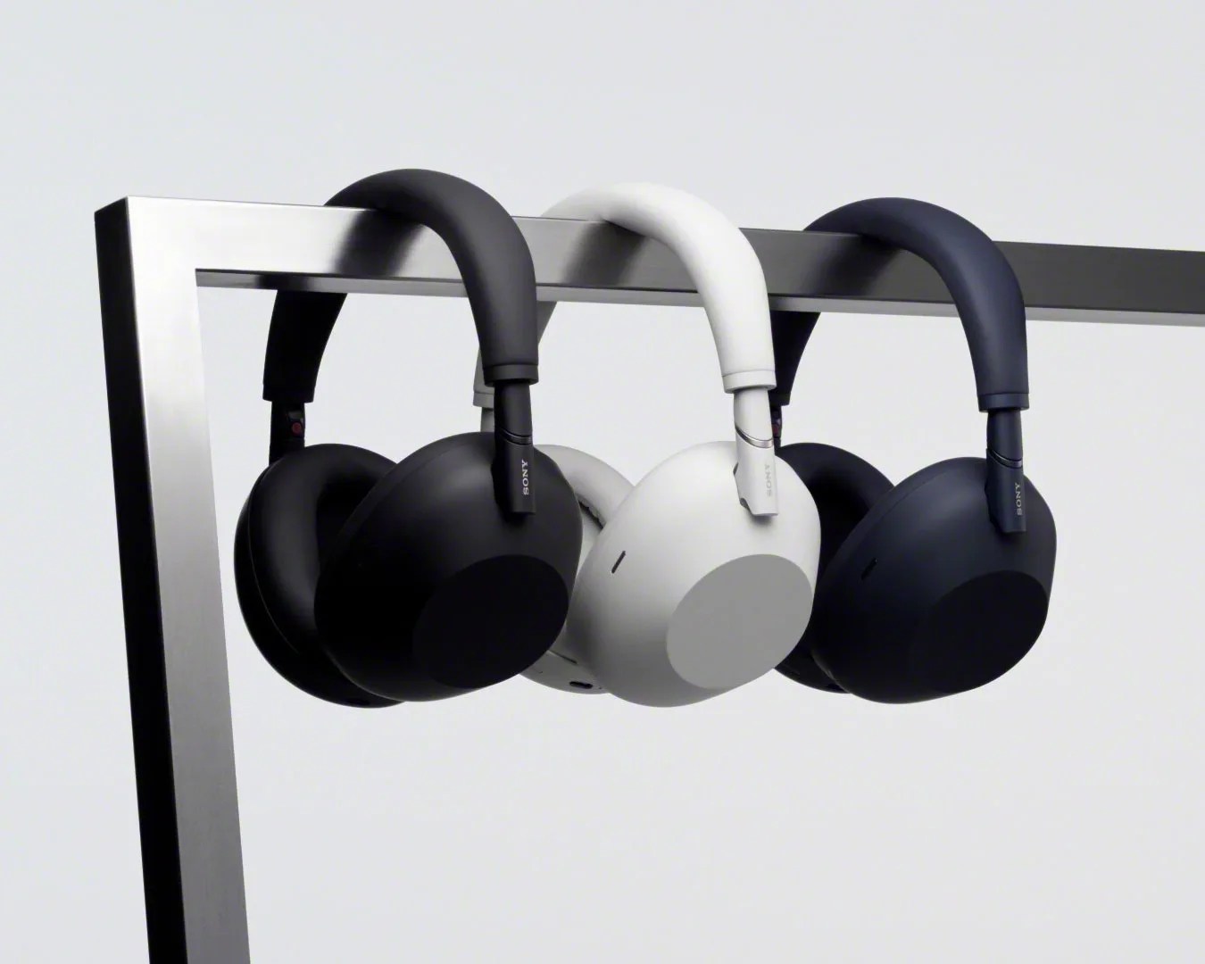 Three Sony wireless over-ear headphones in black, white, and dark blue hanging on a metal rack.