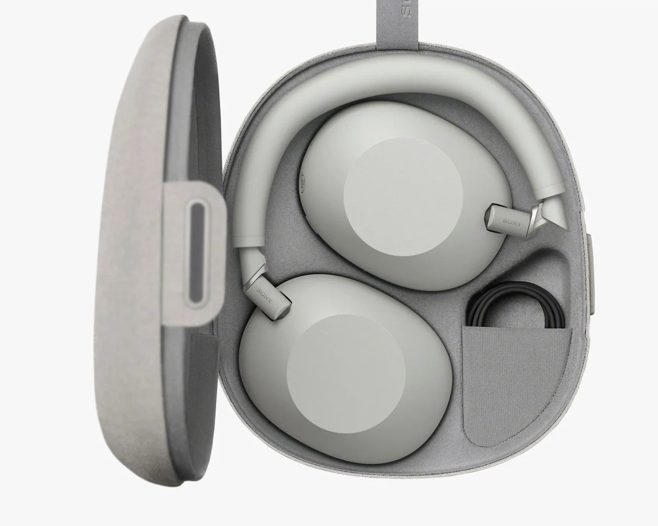 Light gray over-ear headphones neatly folded inside a matching hard carrying case with a coiled black cable in a side pocket.
