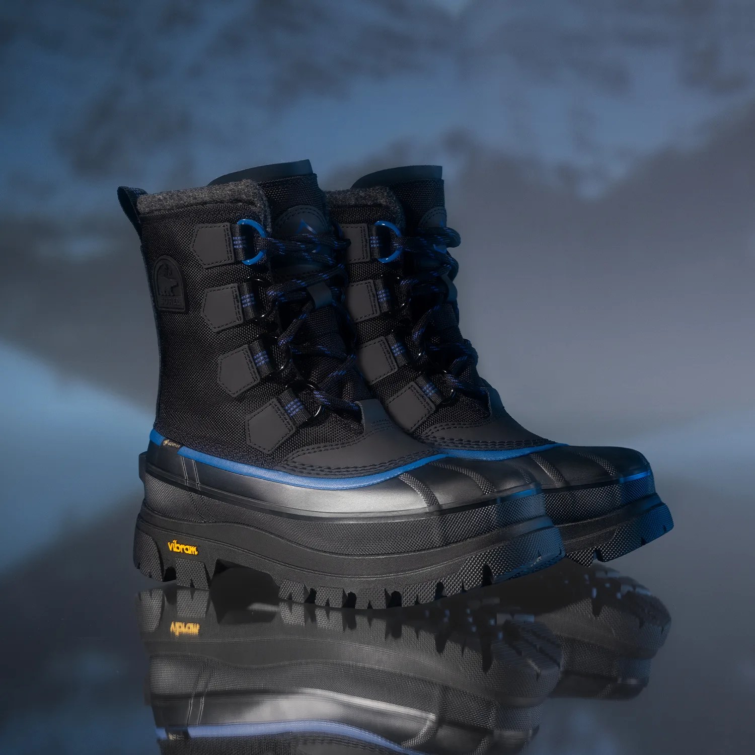 Pair of black and blue insulated winter boots with Vibram soles on reflective surface.