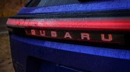 Rear close-up of a blue Subaru car with illuminated red taillight and water droplets on the surface.