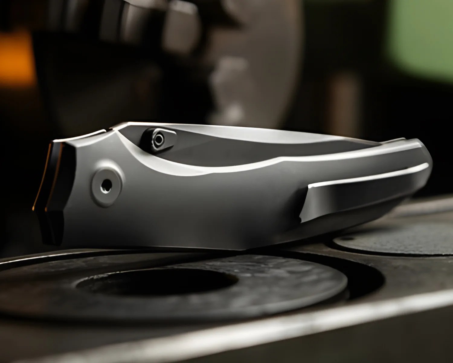 Closed sleek silver folding knife with a clip resting on a dark surface.