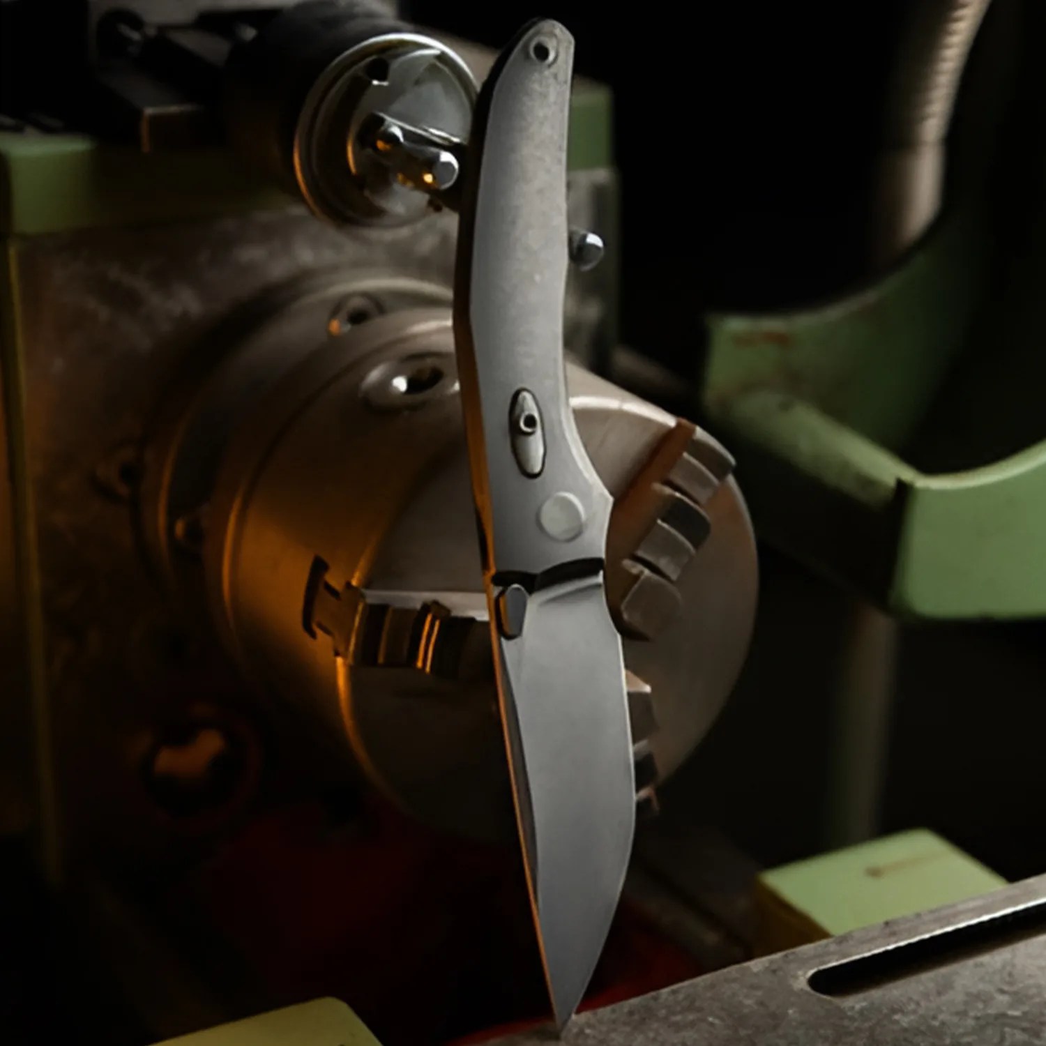 Matte-finished folding knife with a clip point blade held in a metal lathe chuck.