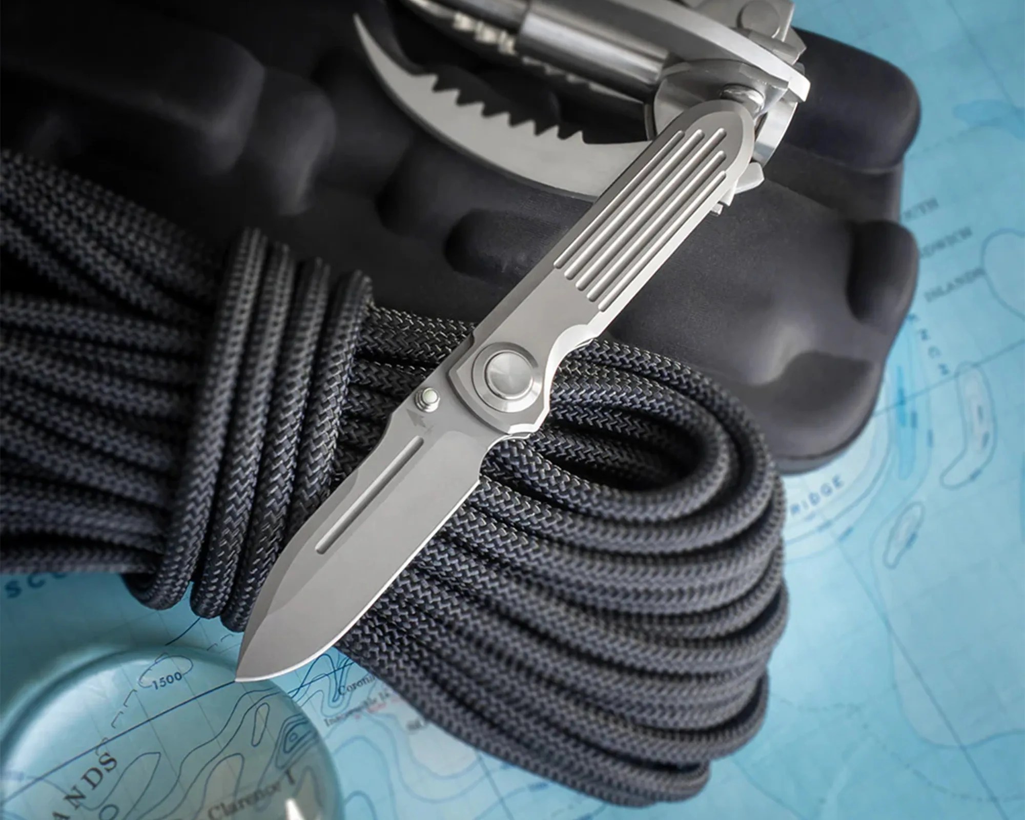 Silver folding knife with grooved handle resting on coiled black rope and a blue map.