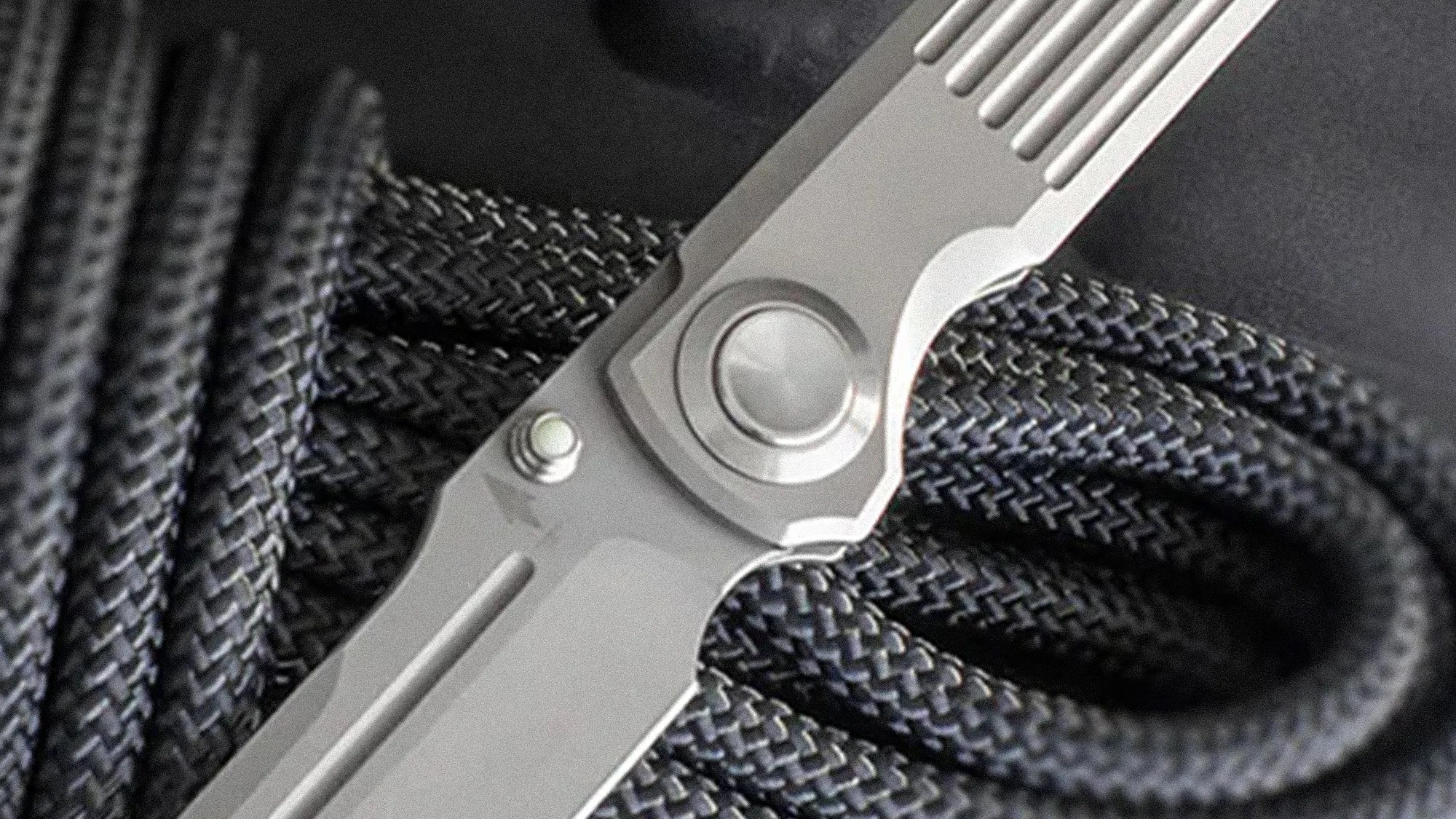 Close-up of a silver folding knife hinge resting on coiled black braided rope.