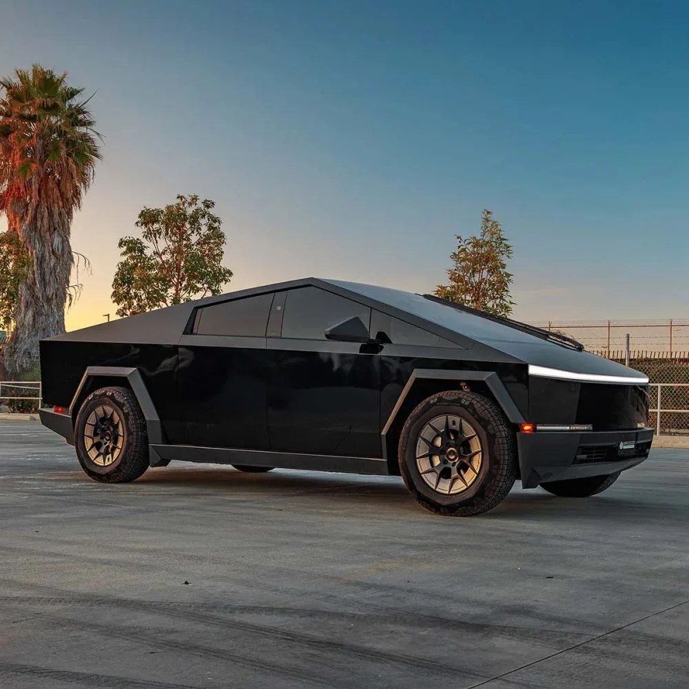 Black angular electric pickup truck with bronze wheels parked on concrete at sunset.