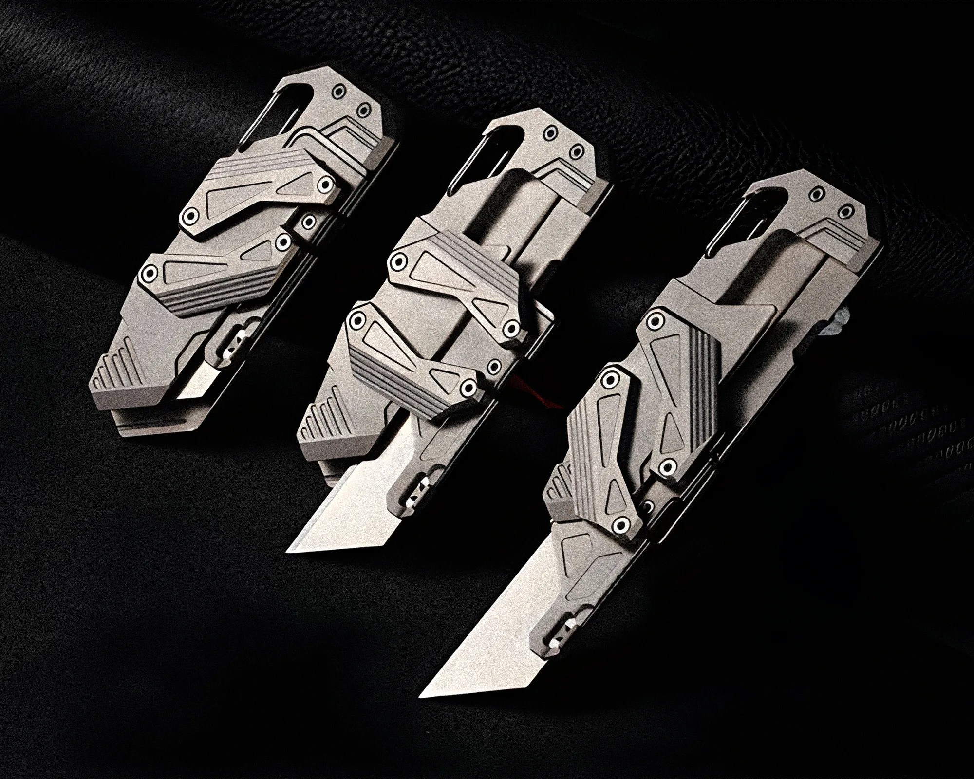 Three futuristic silver folding knives with angular designs and partially open blades on a black surface.