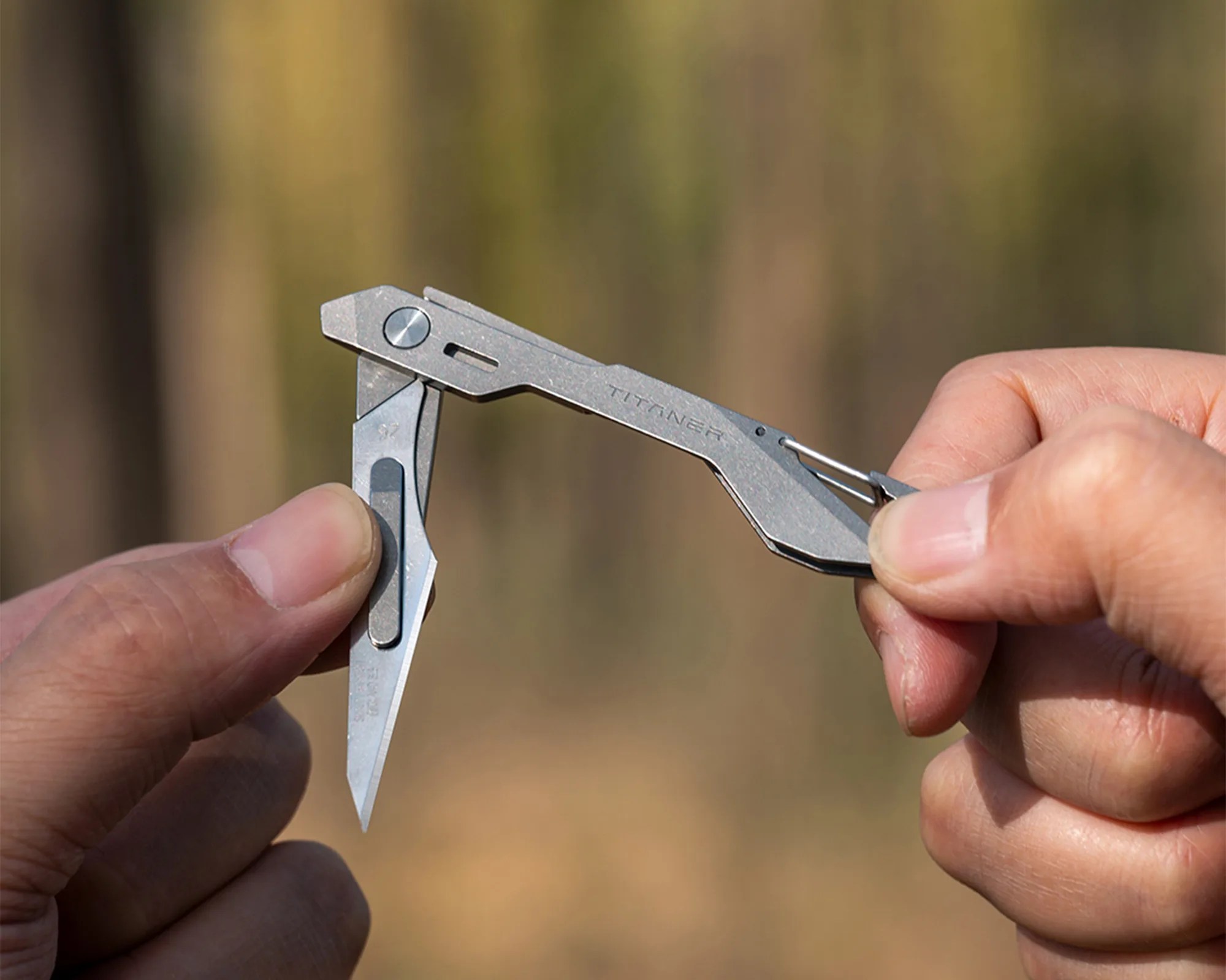 Titaner branded compact titanium folding knife held open between two hands.