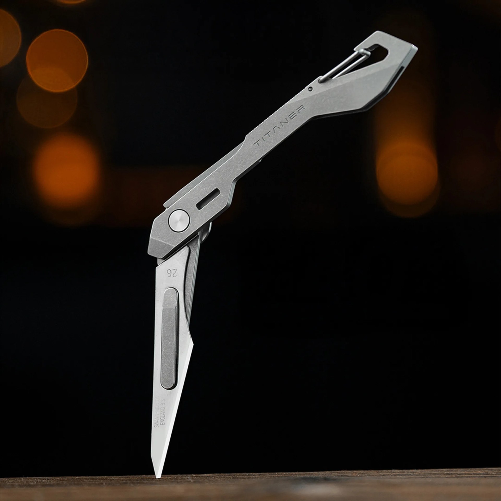 Compact silver titanium folding knife with a clip, partially open on a wooden surface.