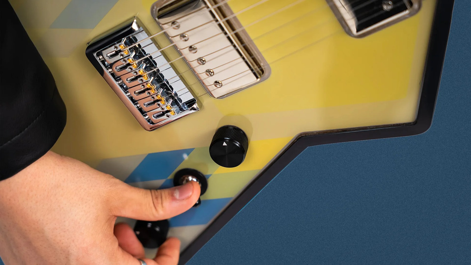 Hand adjusting a knob on a yellow electric guitar with chrome bridge and pickups.