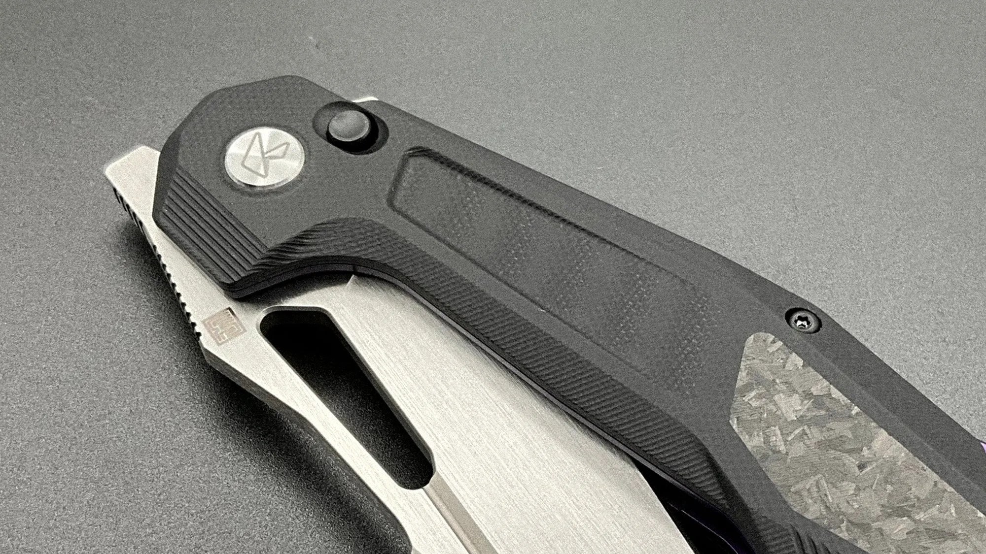 Folding knife with black textured handle and partially visible silver blade on a gray surface.