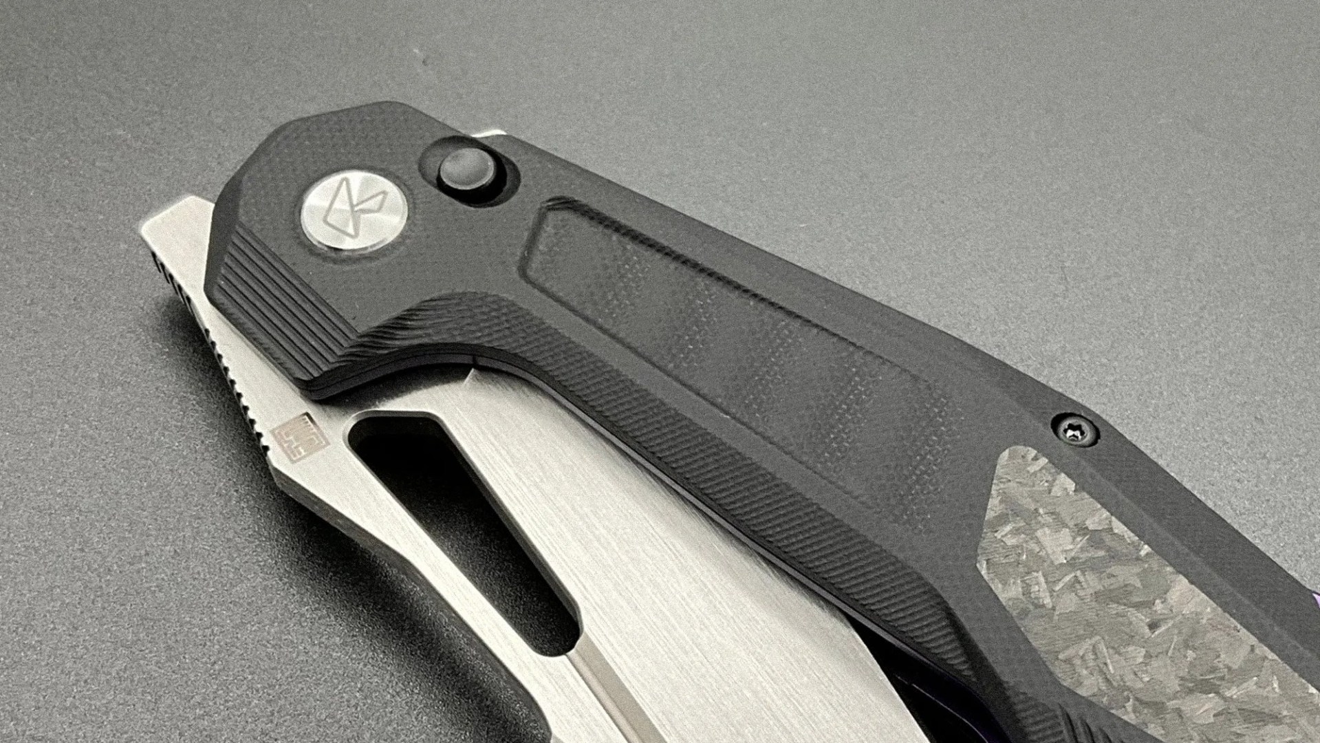 Folding knife with black textured handle and partially visible silver blade on a gray surface.