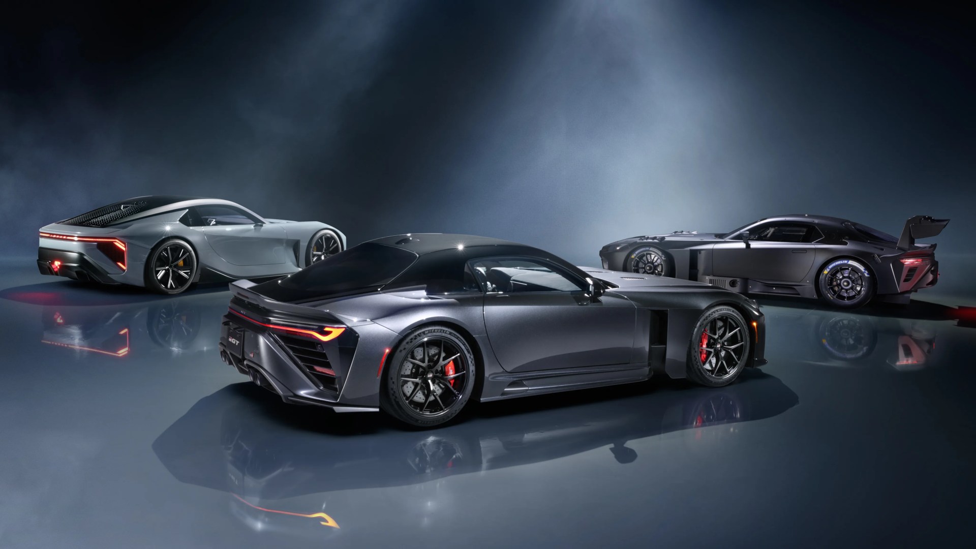 Three sleek, modern sports cars in metallic gray shades on a reflective floor with a dark, smoky background.