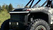 Front side view of a rugged off-road vehicle with digital camouflage paint, large knobby tires, and coil suspension.
