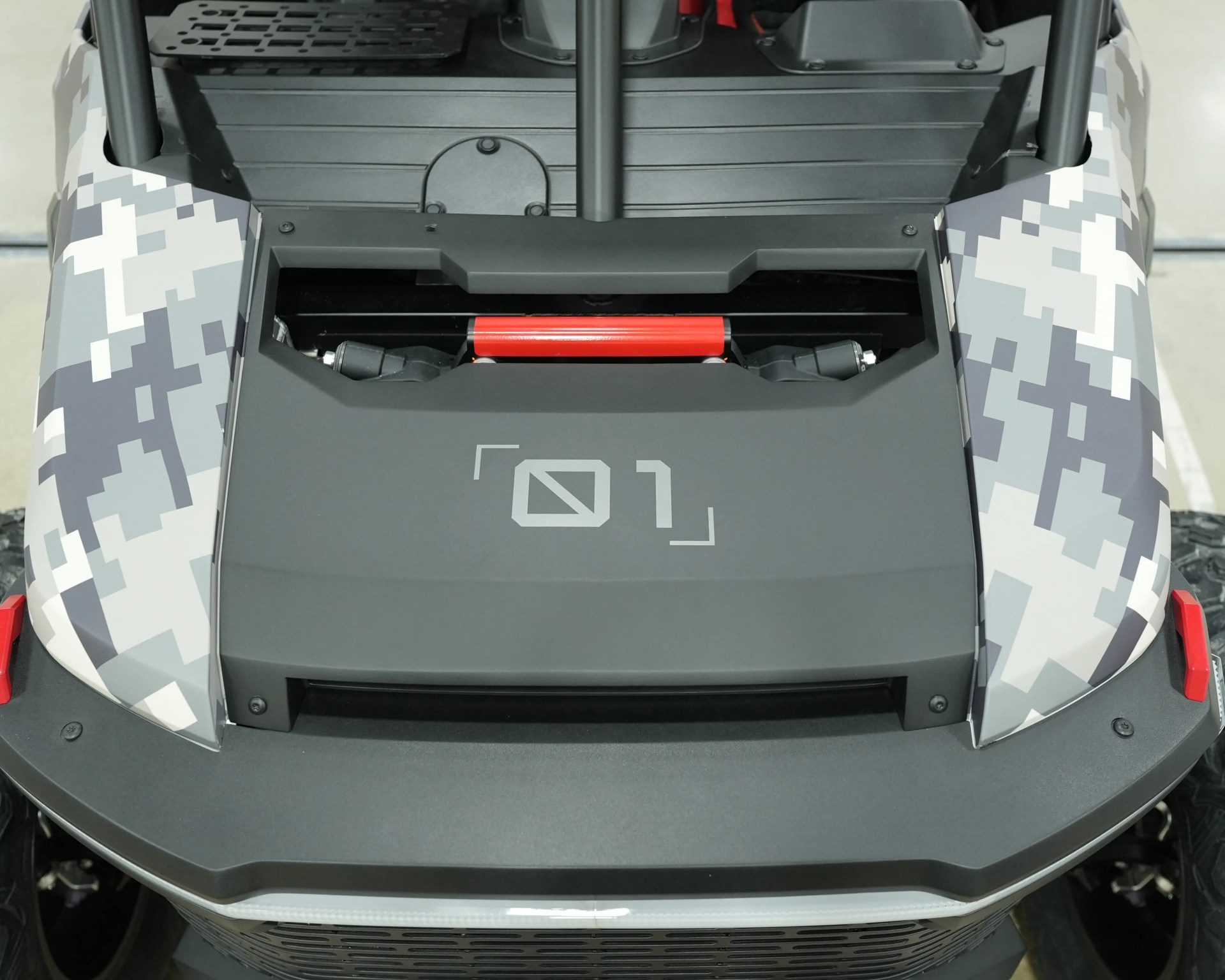 Front section of a vehicle with digital camouflage fenders and a matte black hood featuring a red bar and a symbol resembling "01".