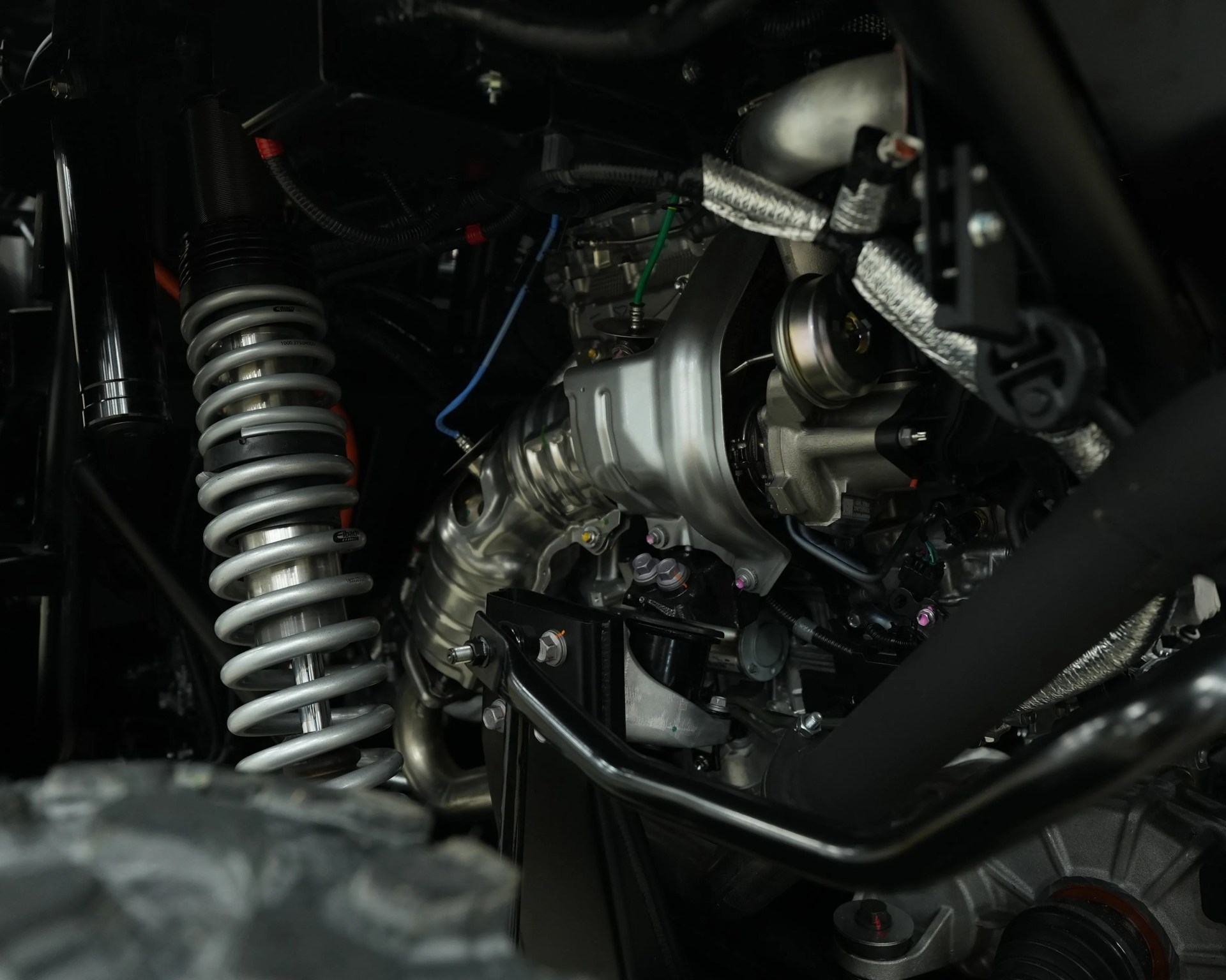 Close-up of a silver coil spring suspension and engine components inside a vehicle chassis.