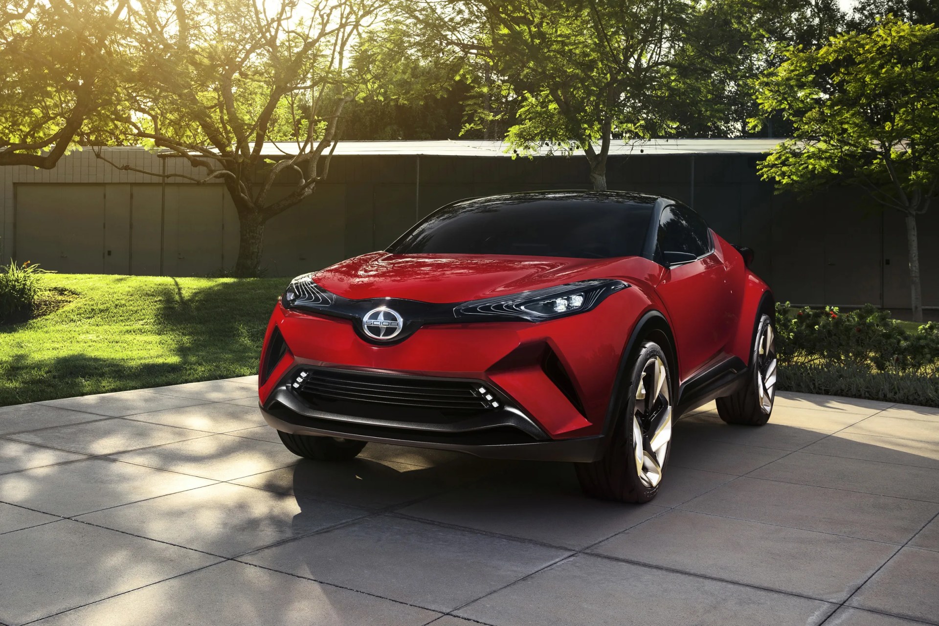 Red Scion concept car with black roof and futuristic design parked on a tiled driveway with trees in the background.