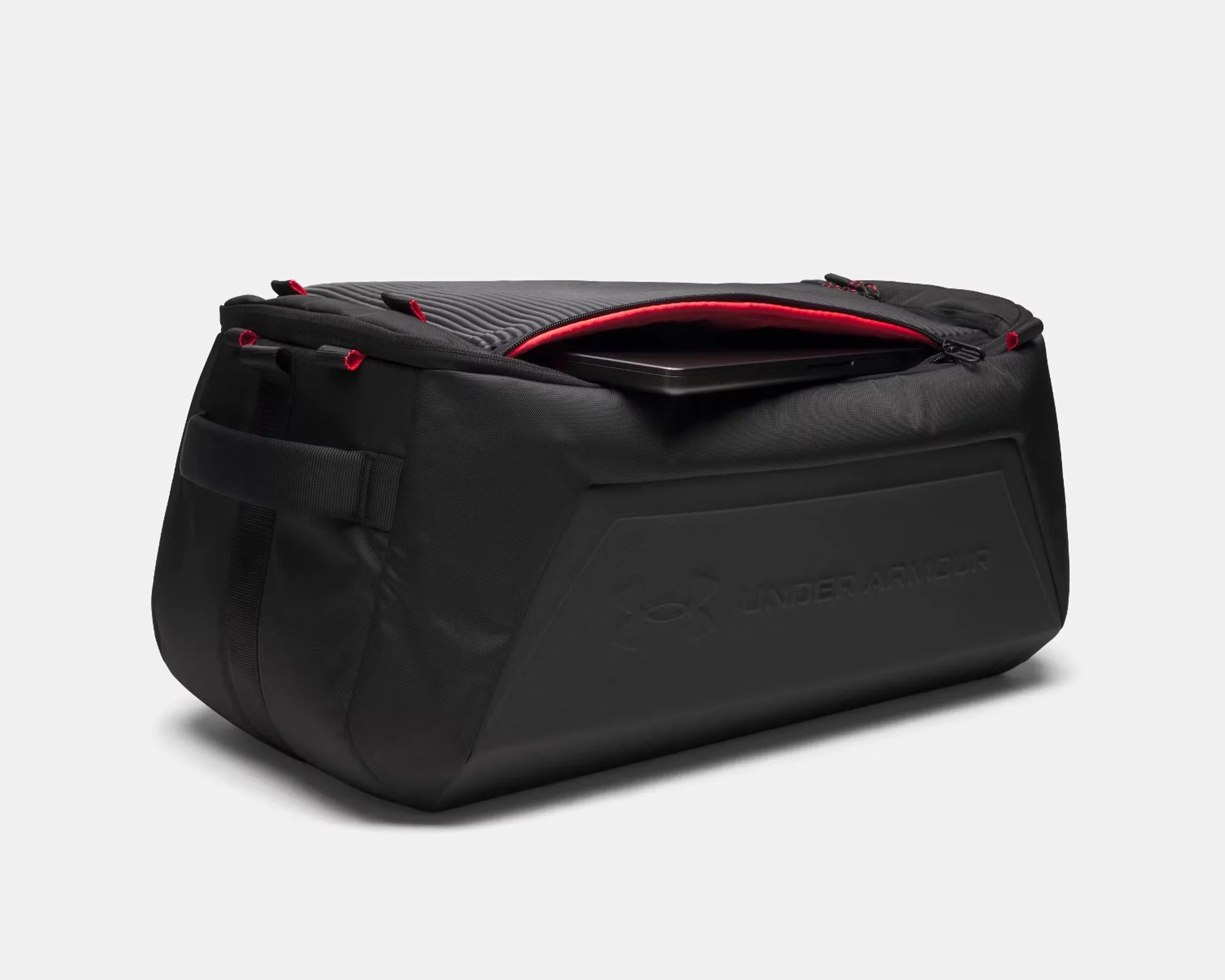Black Under Armour duffel bag with red zipper lining partially open showing a laptop inside.