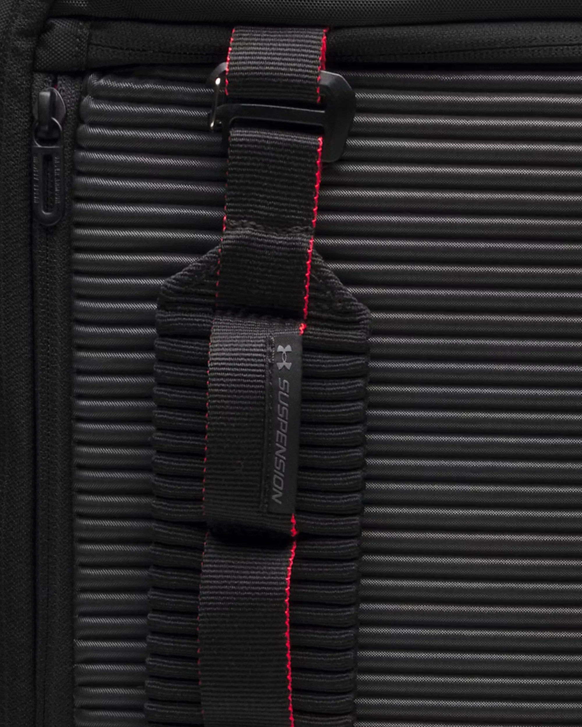 Close-up of a black textured bag with a black strap featuring red stitching and a label reading "Suspension.