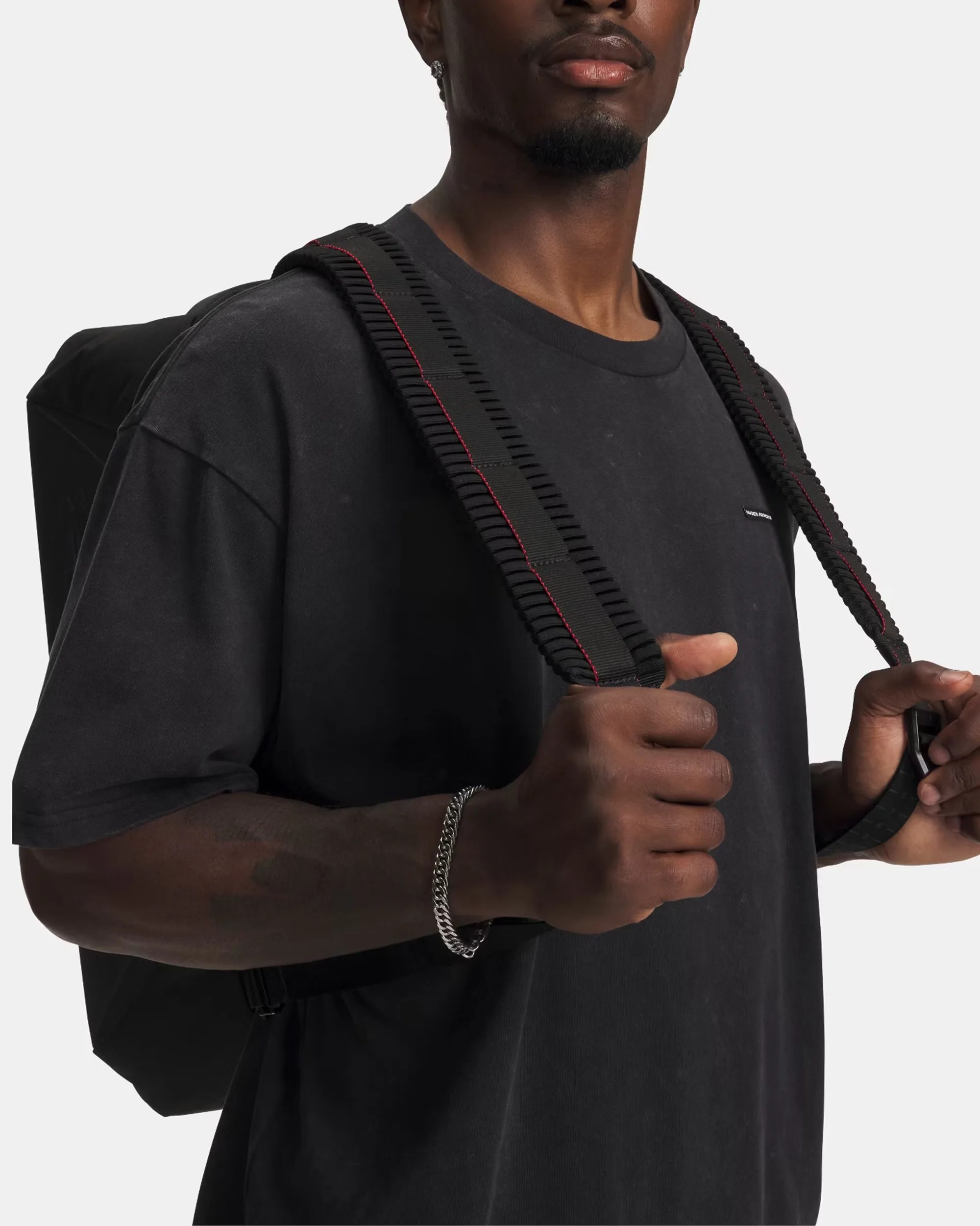 Black backpack with padded shoulder straps featuring red stitching worn by a person in a black t-shirt.