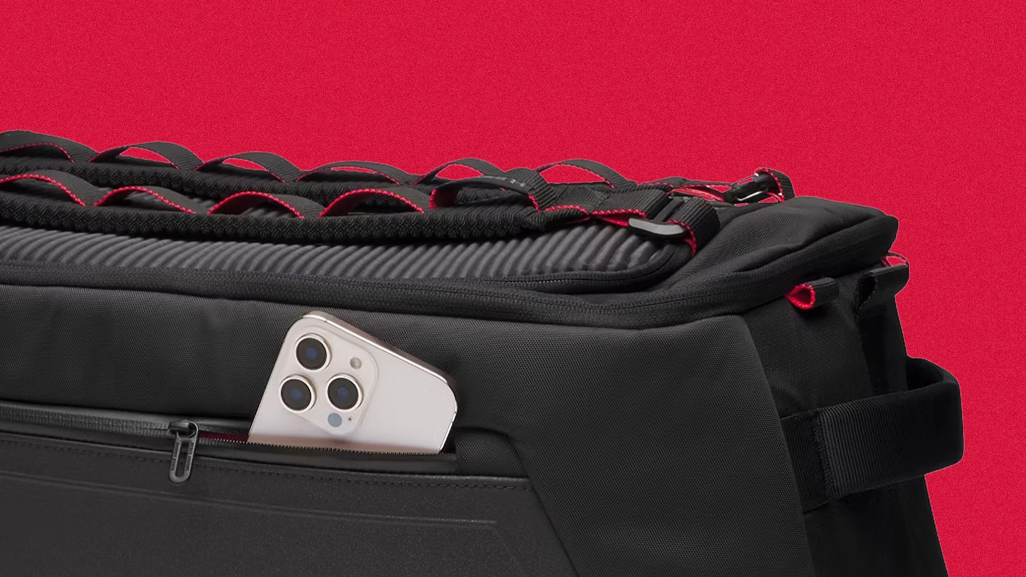 Black padded bag with red trim and a white smartphone partially visible in a side pocket.
