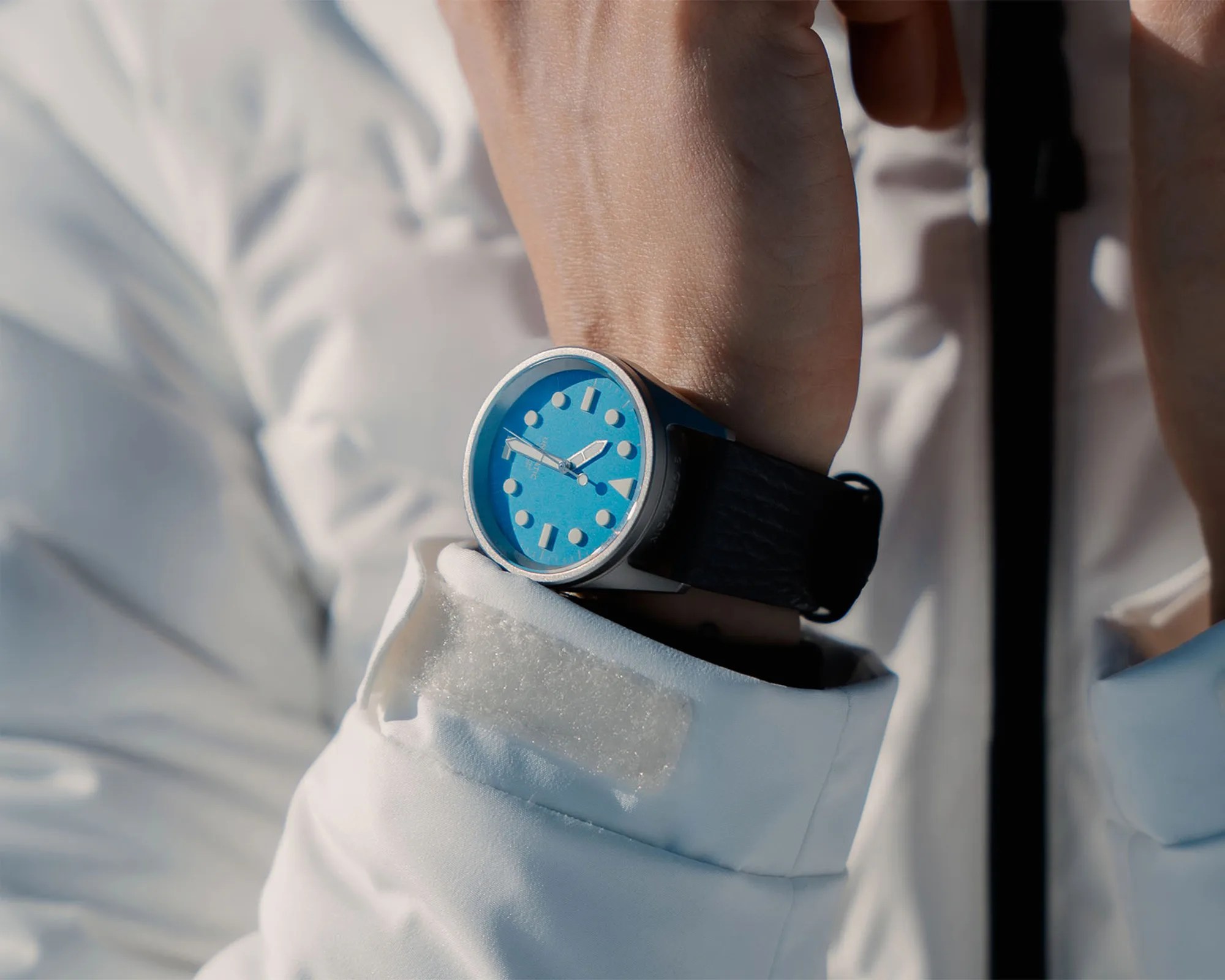 Wristwatch with a bright blue dial and black leather strap worn over a white jacket cuff.