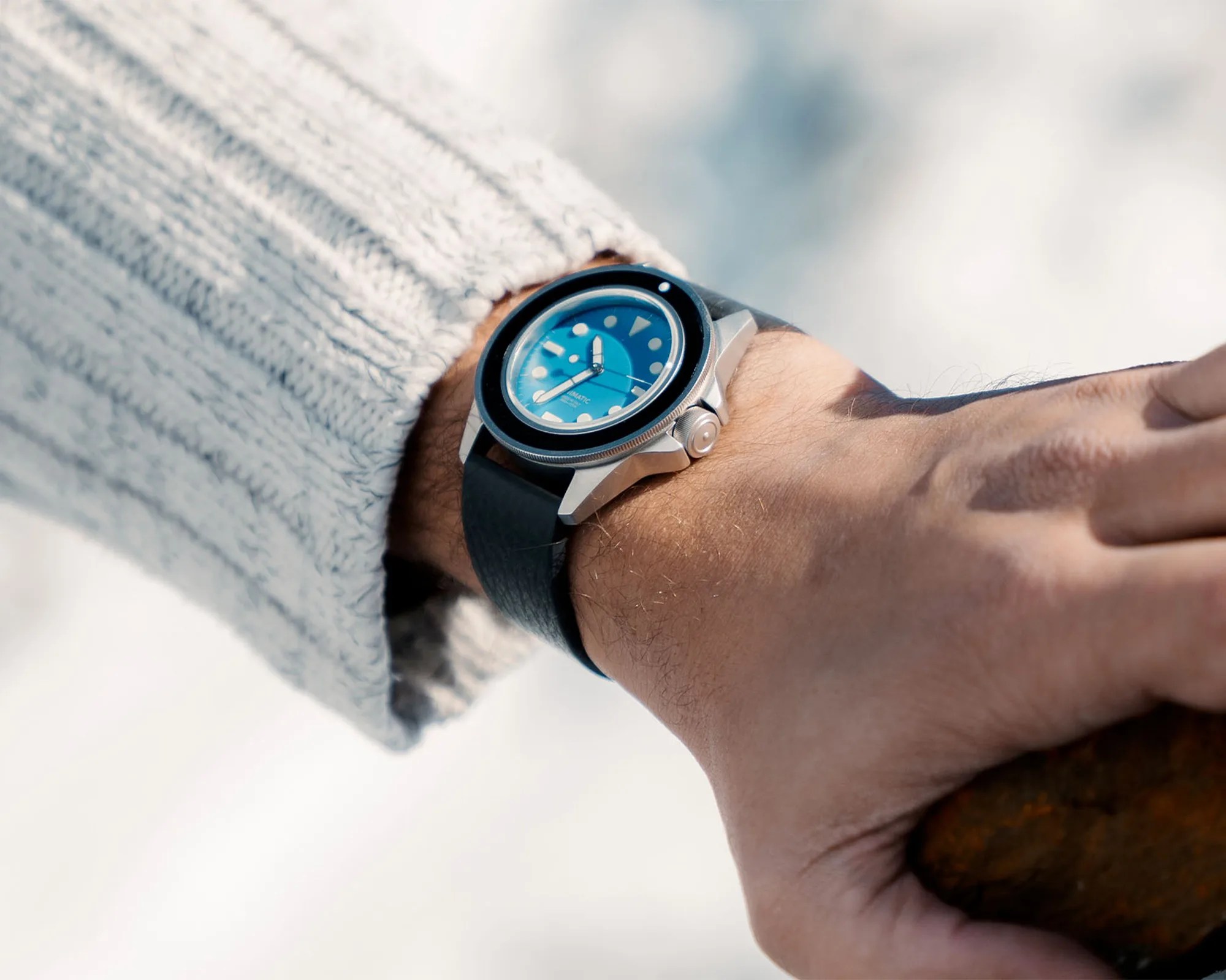 Silver wristwatch with a blue dial and black leather strap worn on a wrist with a light gray knitted sweater.