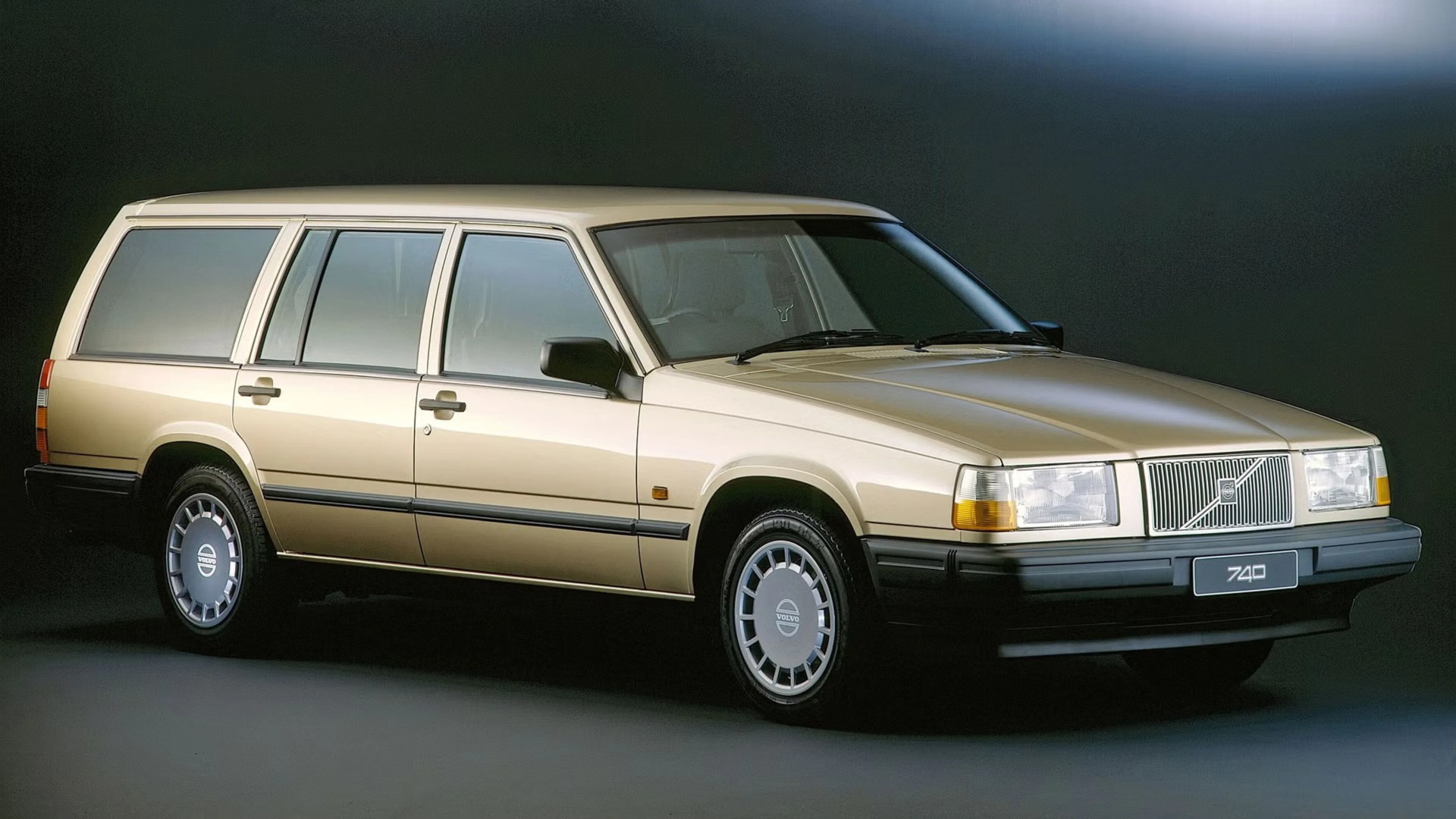 Beige Volvo 740 station wagon with black trim and silver hubcaps on a dark background.