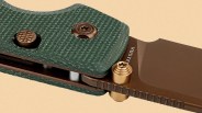 Close-up of a green textured knife handle with bronze screws and a bronze blade marked "VOSTEEL.