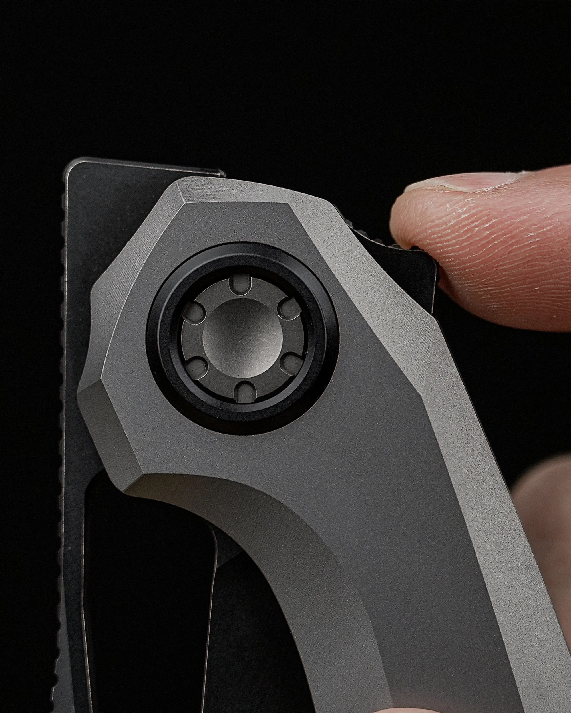 Close-up of a finger holding the pivot area of a gray folding knife with a black blade.