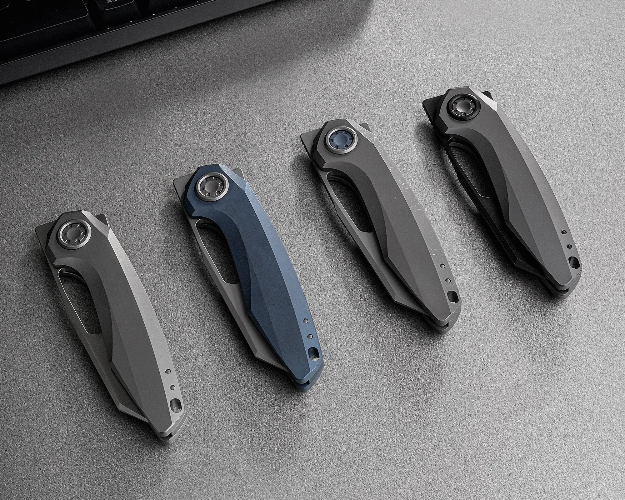Four closed folding knives with angular handles in gray and blue, arranged in a row on a gray surface.