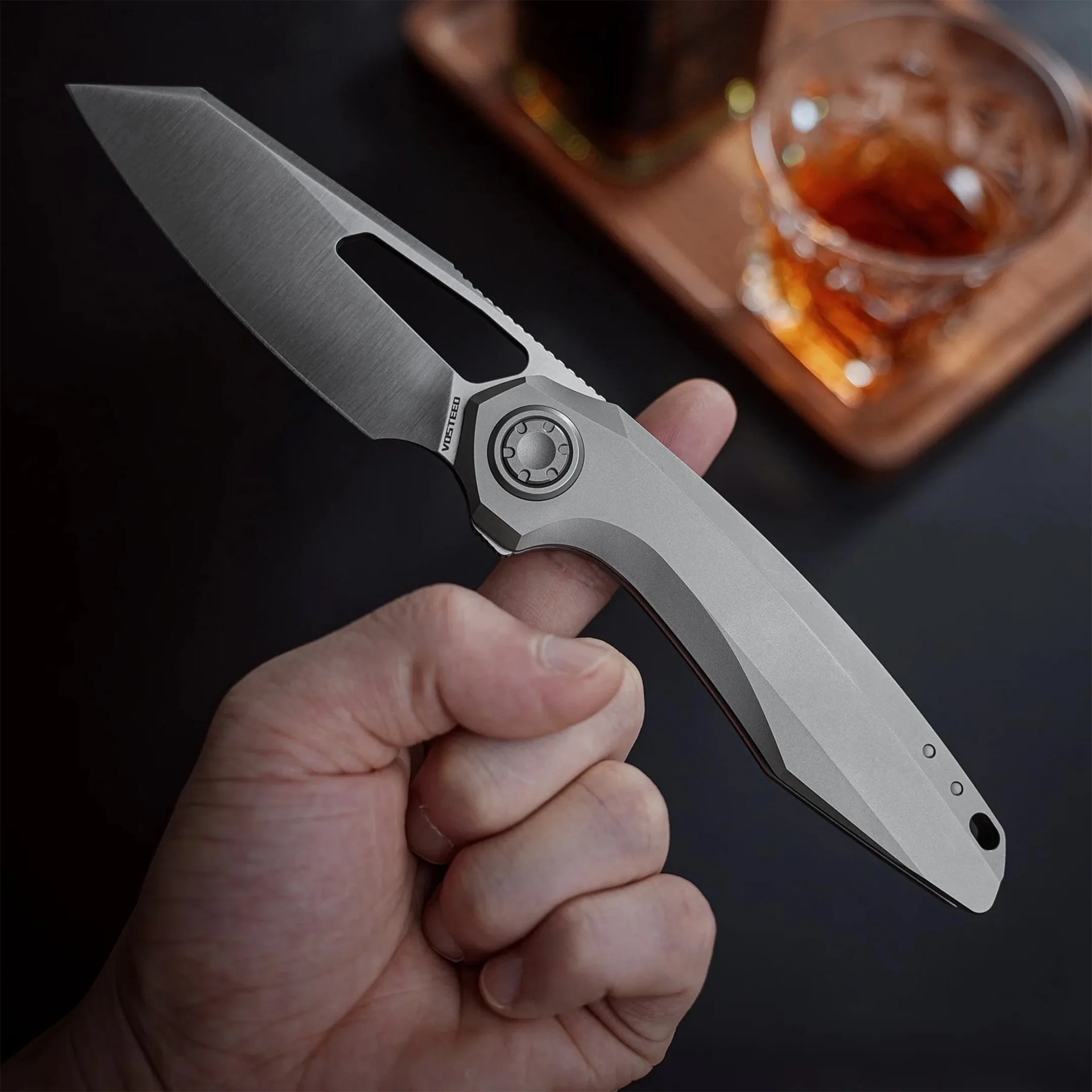 Hand holding a sleek, silver folding knife with a partially open blade and a geometric handle design.