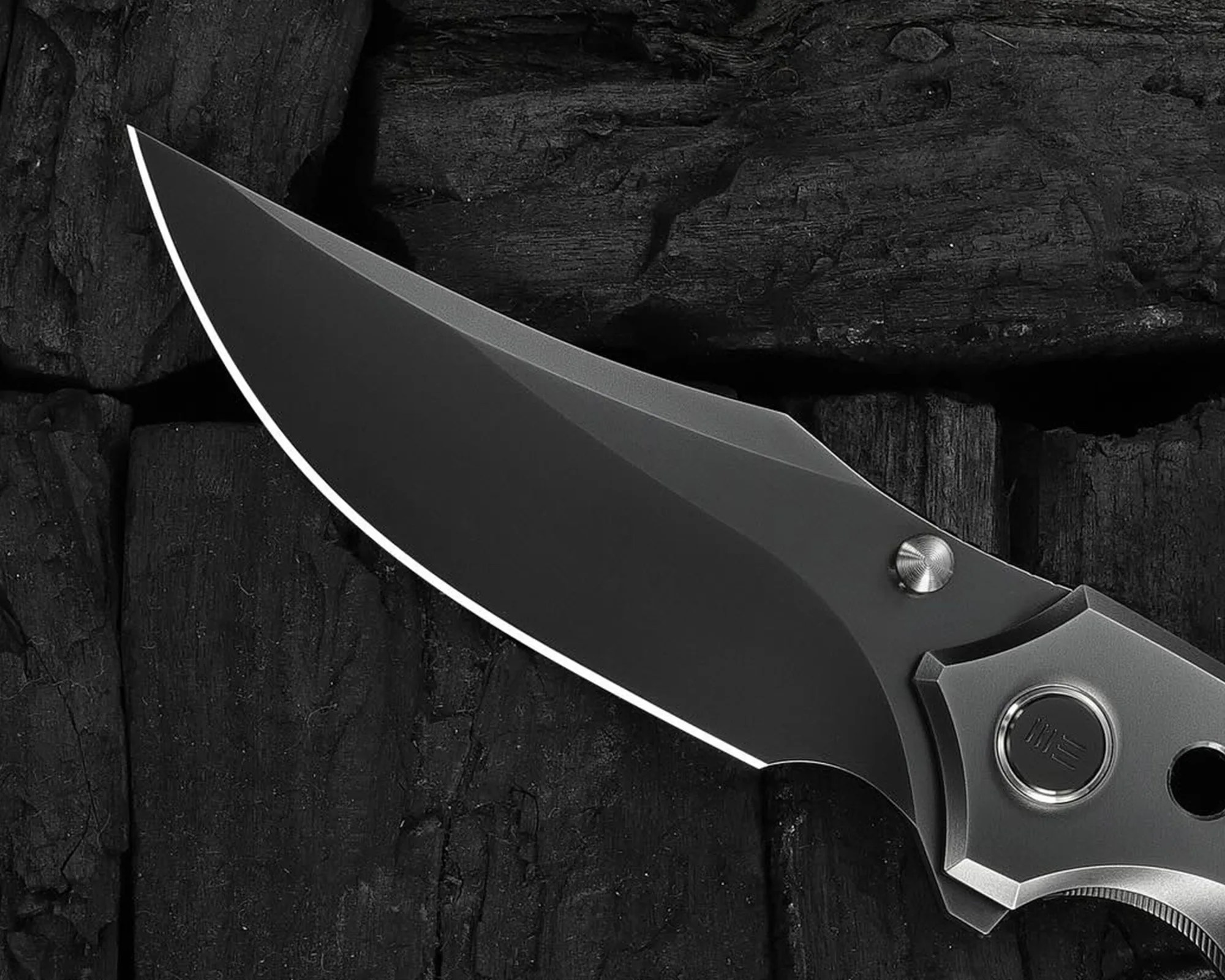 Close-up of a sleek black folding knife blade with a matte finish on a dark textured wooden surface.