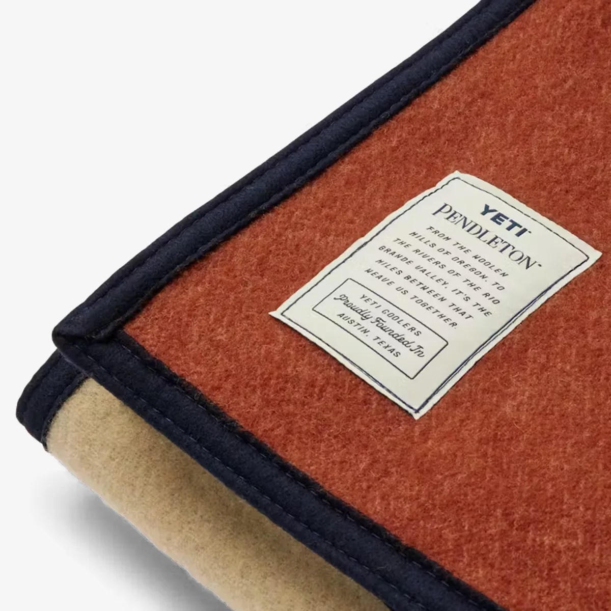 Folded wool blanket in rust and beige with navy blue trim and a white YETI Pendleton label.