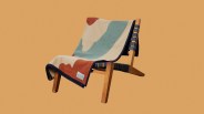 Wooden lounge chair with black straps and a multicolored abstract-patterned blanket draped over it.