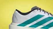 Close-up of a white Adidas Adizero Evo SL shoe with teal stripes and gray laces against a yellow background.