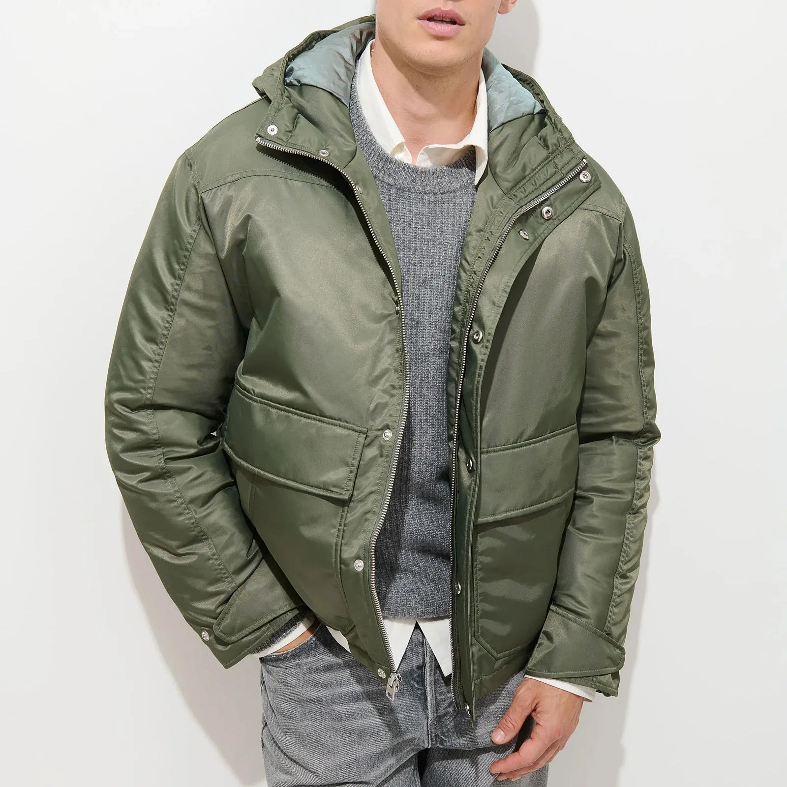 Olive green padded jacket with zipper and snap buttons worn over a gray sweater and white shirt.