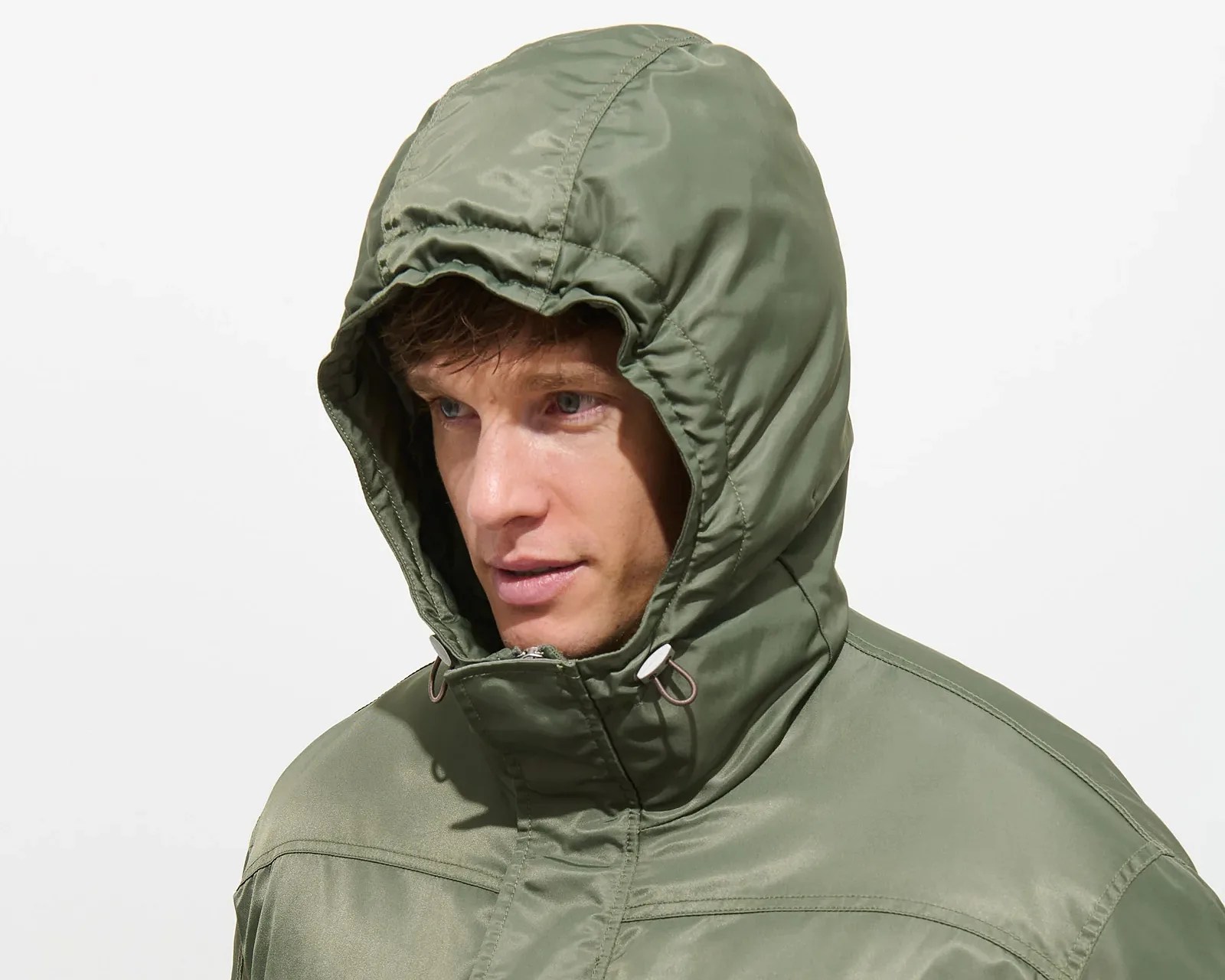 Man wearing an olive green hooded jacket with drawstring toggles near the chin.