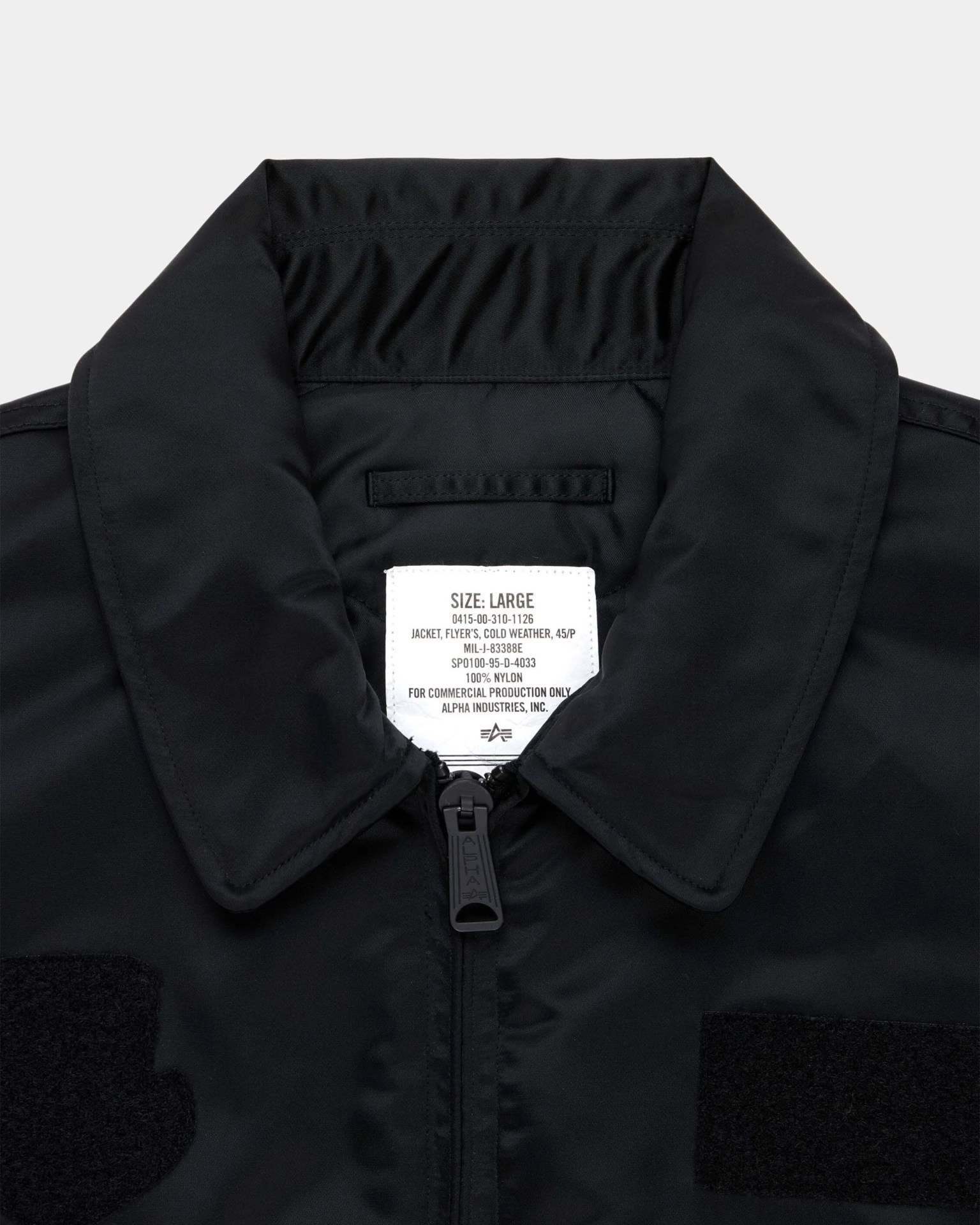 Close-up of a black nylon cold weather jacket collar with a visible white size label and a black zipper pull.