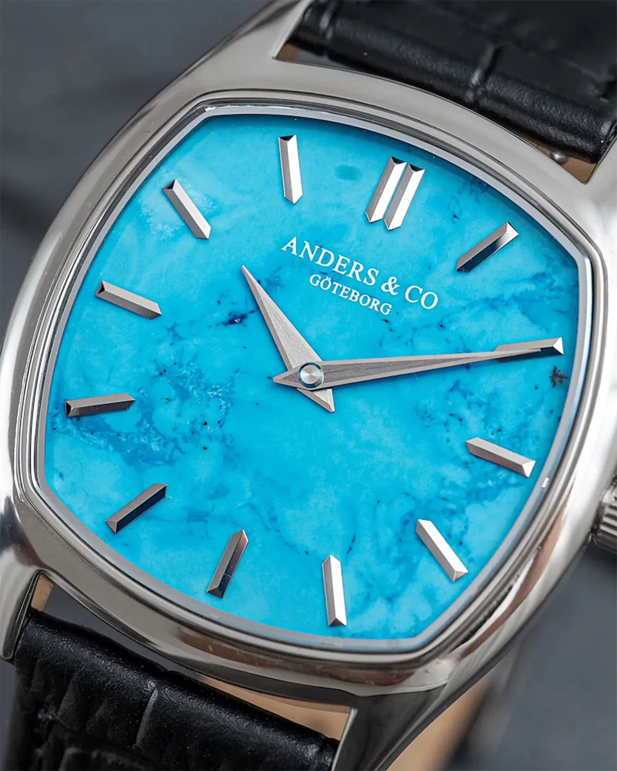 Silver watch with a bright blue marbled dial, silver hour markers, and black leather strap.