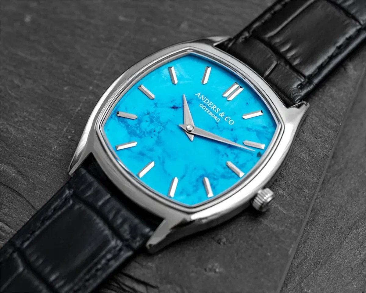 Silver wristwatch with a bright blue marbled dial and black leather strap on a dark textured surface.