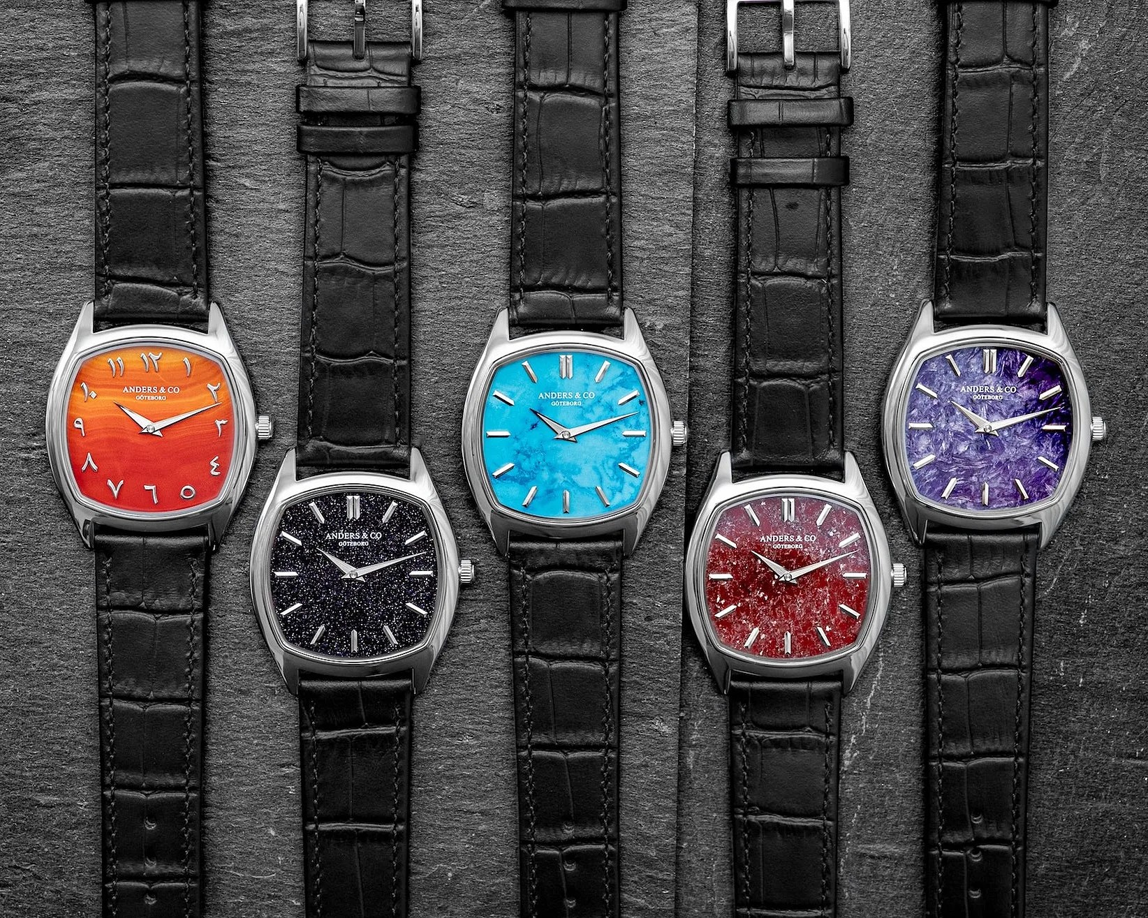 Five Anders & Co wristwatches with black leather straps and square silver cases, featuring orange, black, turquoise, red, and purple textured dials.