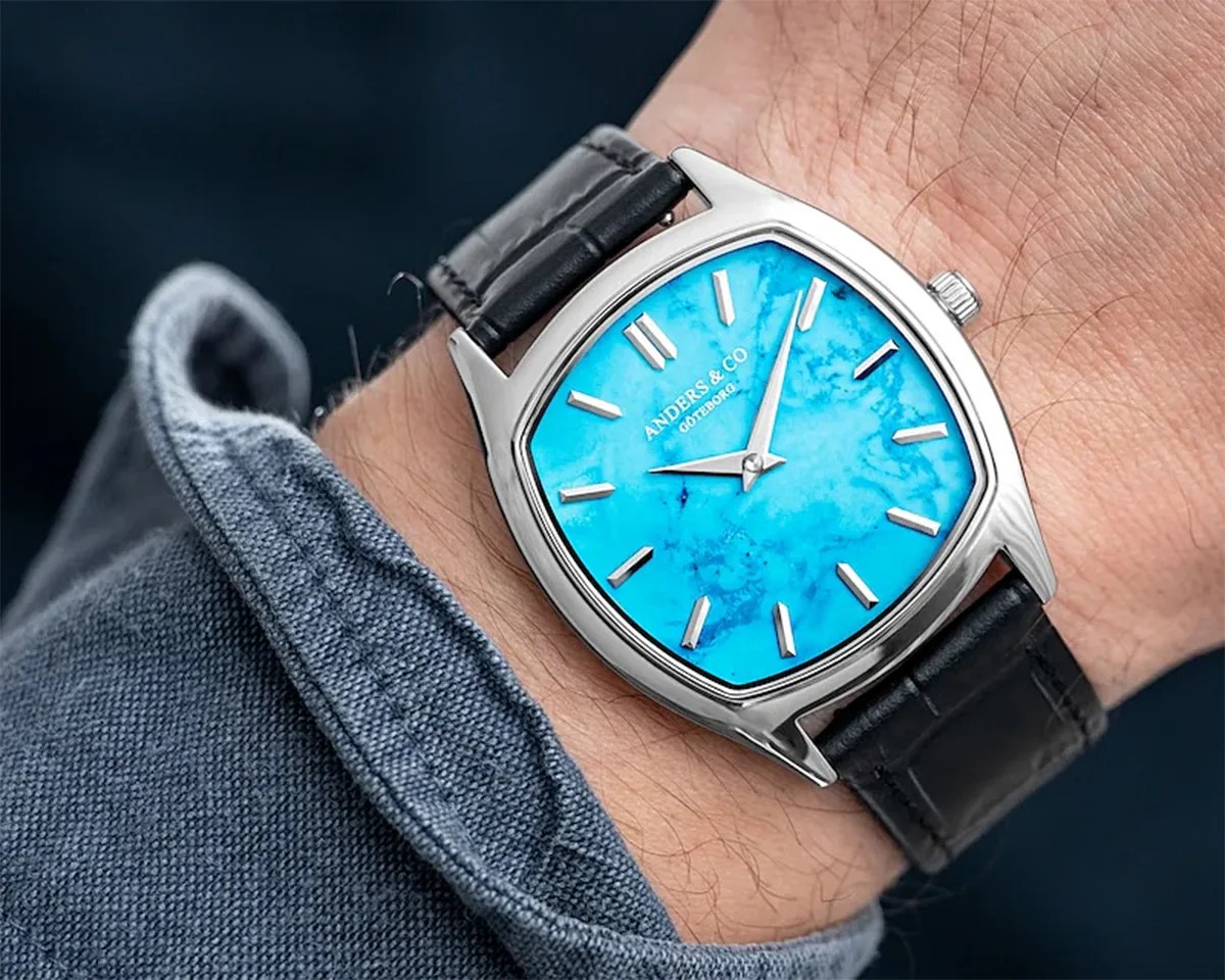 Silver watch with a bright turquoise marbled dial and black leather strap worn on a wrist.
