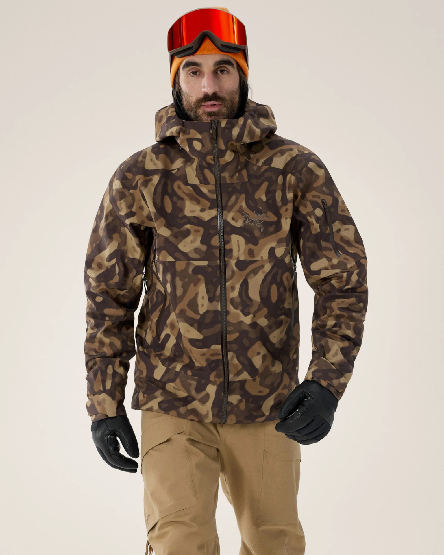 Brown and tan camouflage jacket with hood worn with tan pants and black gloves.