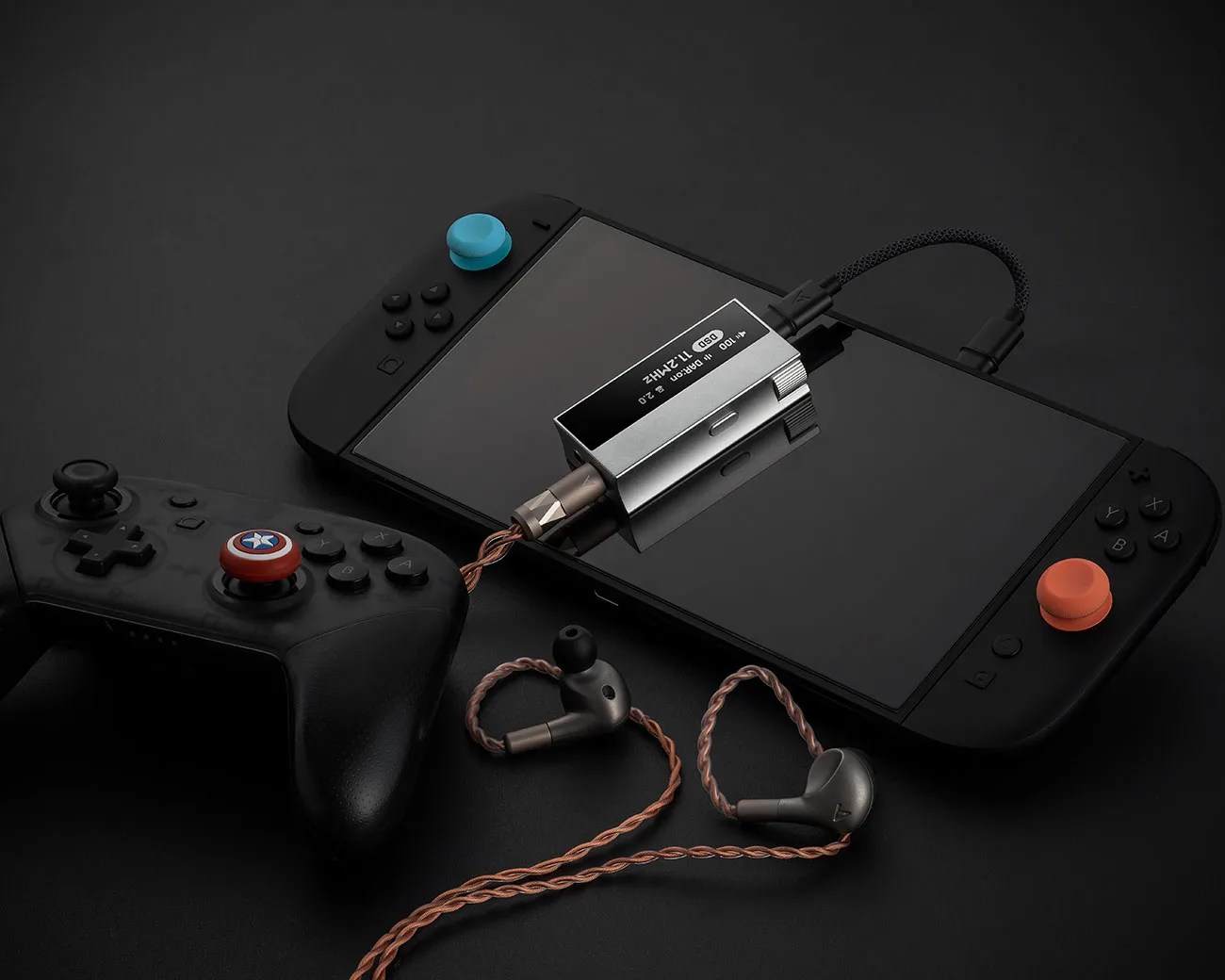 Black handheld gaming console with blue and orange thumbsticks connected to a silver audio device and black wired earphones.