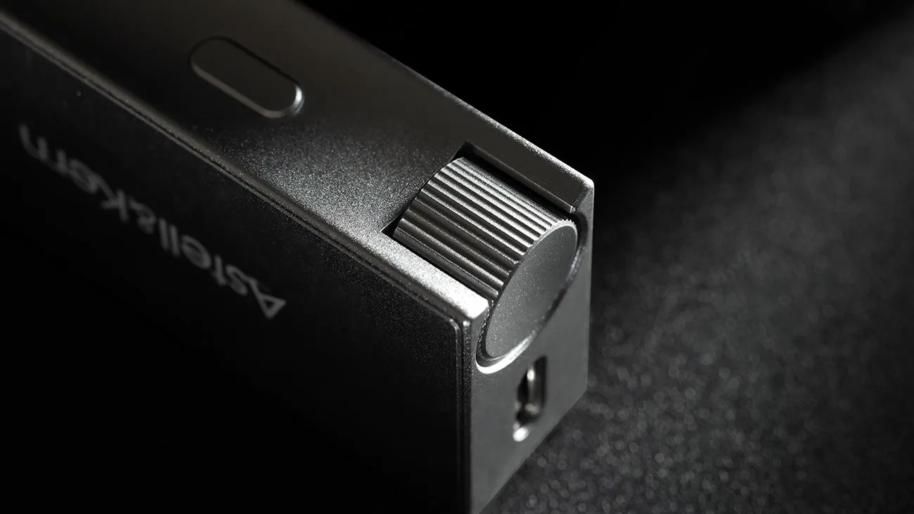 Close-up of a black Astel & Kern device with a textured volume knob and a small button on a dark surface.